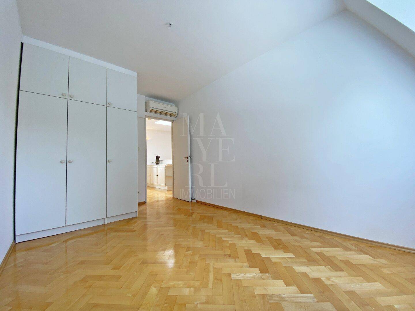 Geräumiges Schlafzimmer mit Fischgrätparkett, Einbauschränken und einer Dachschräge.