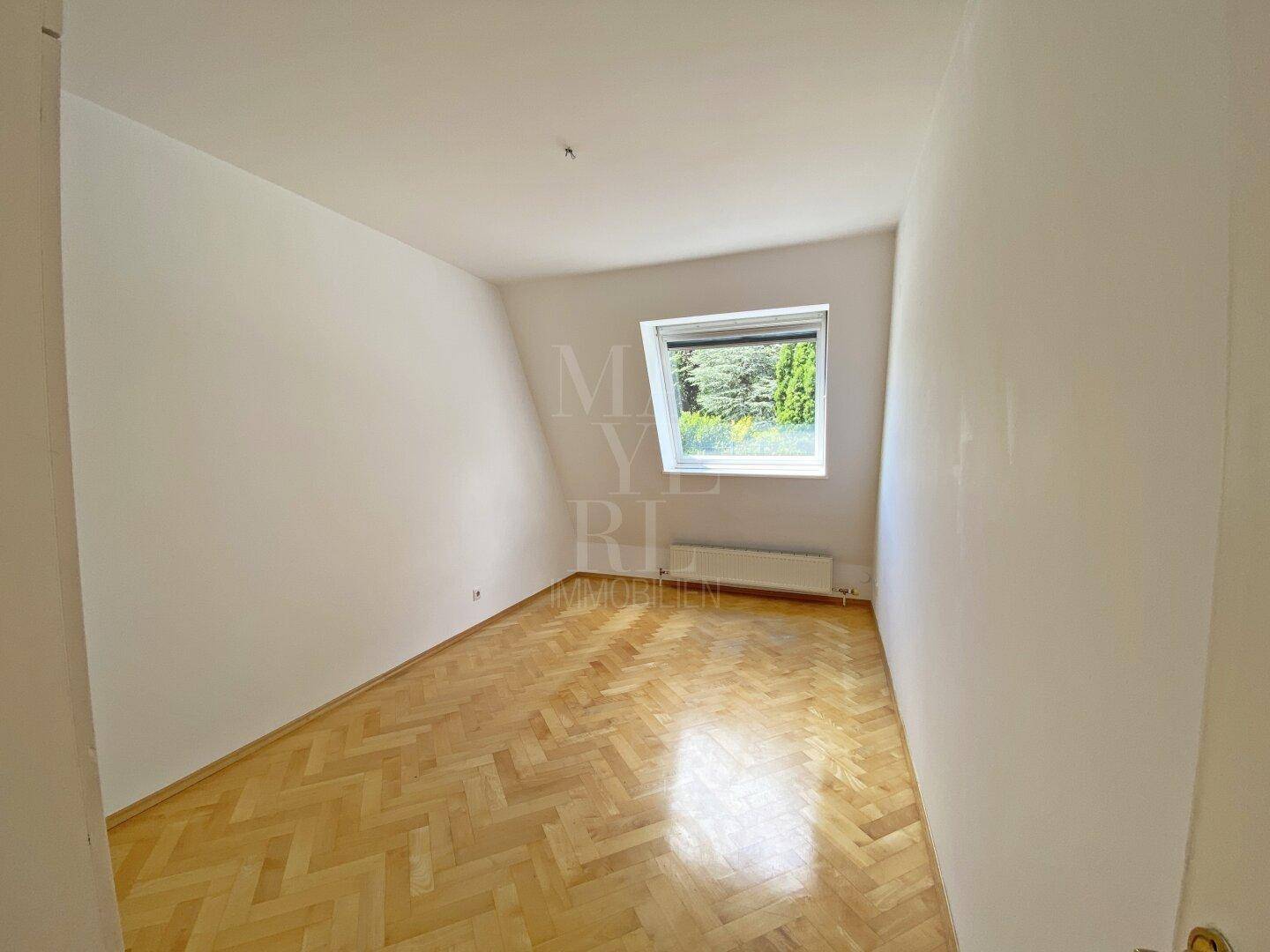 Schlafzimmer mit Fischgrätparkett, weißen Wänden und einem Dachfenster, das viel Licht spendet.