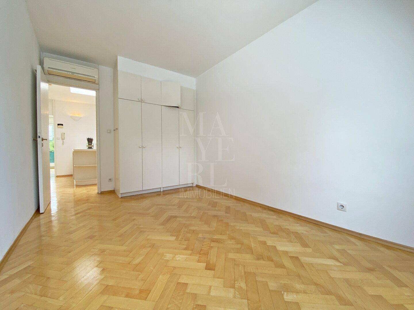 Helles Schlafzimmer mit Fischgrätparkett, Einbauschränken und einer Dachschräge.