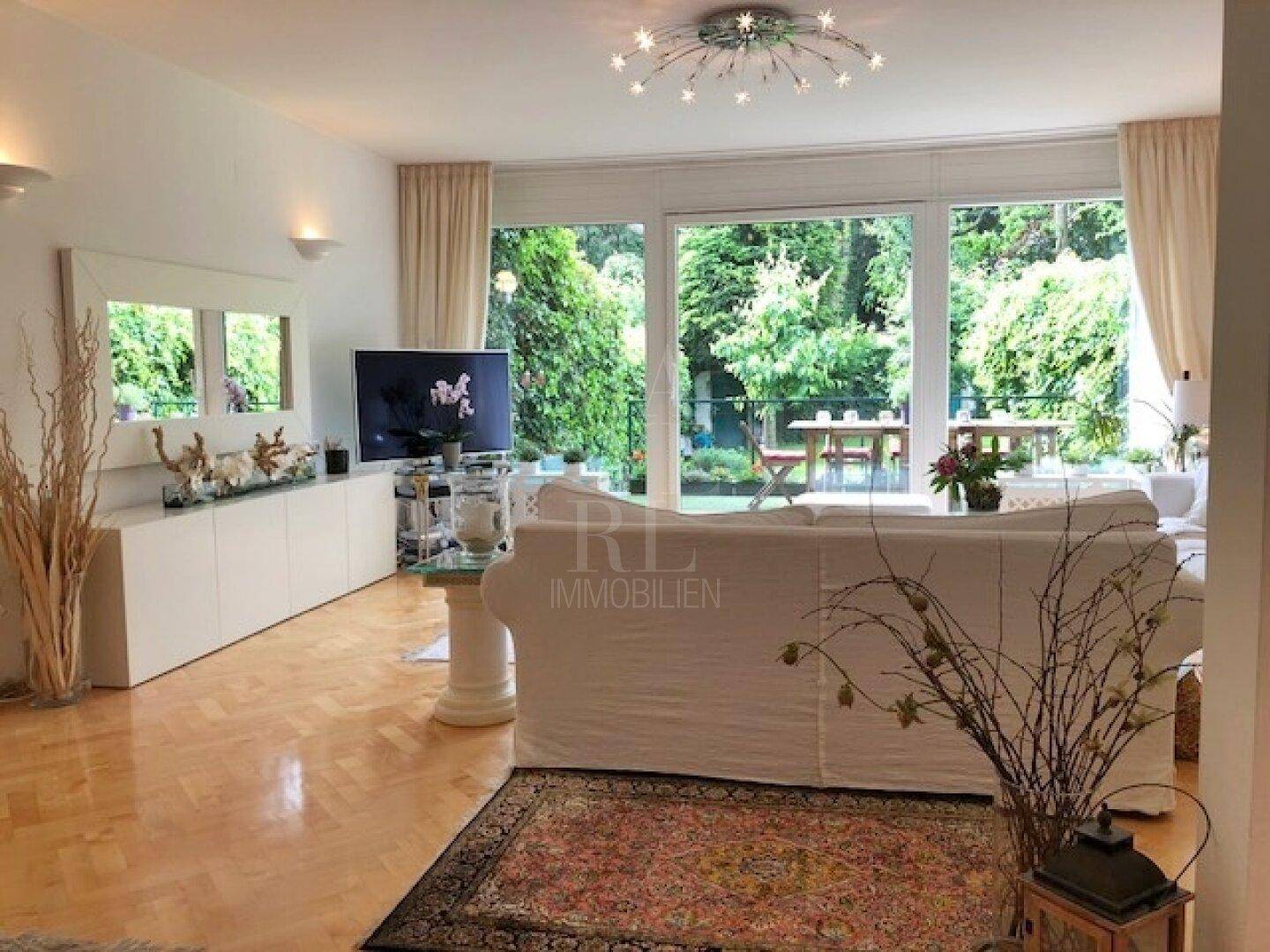 Gemütliches Wohnzimmer mit großem Sofa, Fernseher und weitem Blick in den grünen Garten.