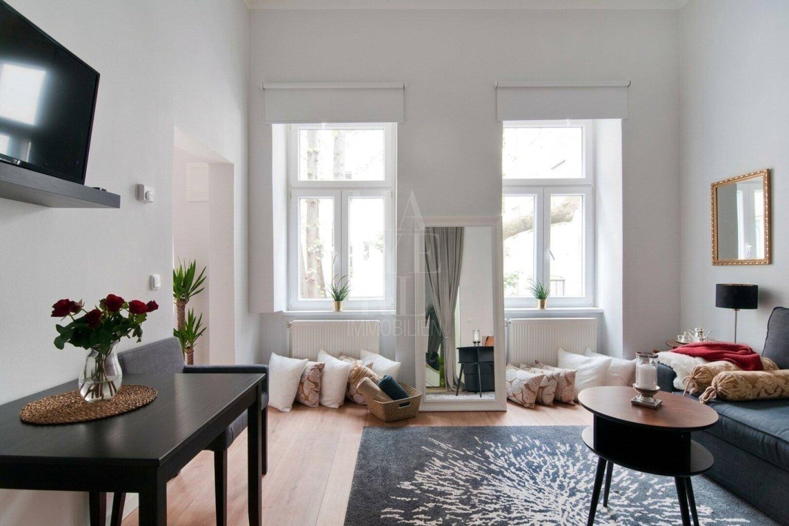 Gemütliches Wohnzimmer mit Holzboden, großem Spiegel und hellen Fenstern zum Innenhof.