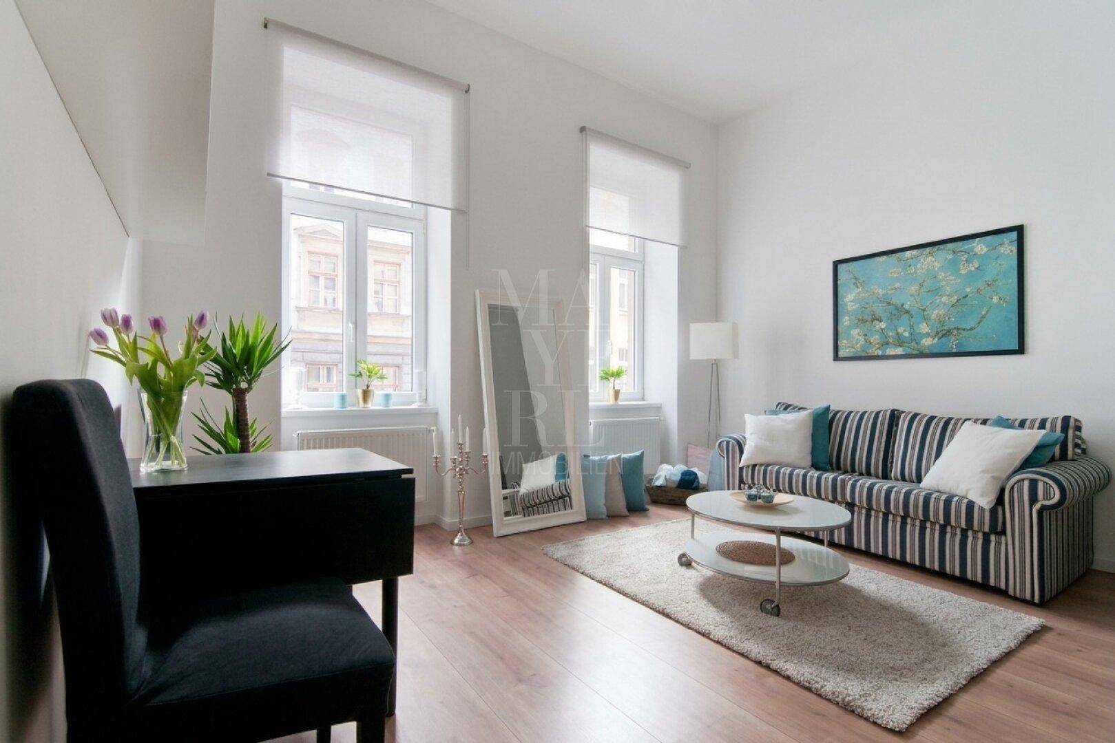 Helles Wohnzimmer mit gestreiftem Sofa, Holzboden und einem Schreibtisch am Fenster.