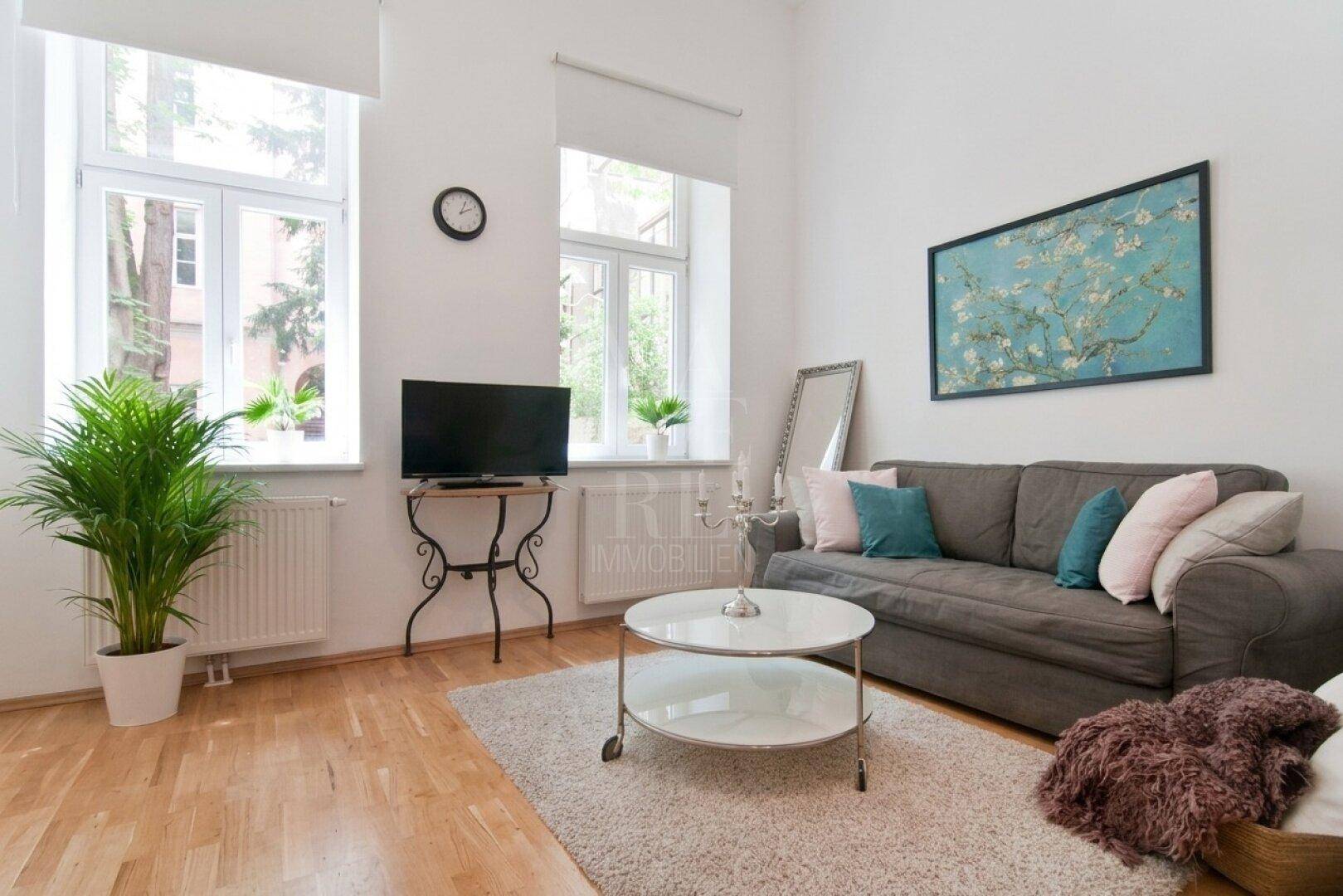 Einladendes Wohnzimmer mit bequemem Sofa, Holzboden und Blick ins Grüne durch die Fenster.