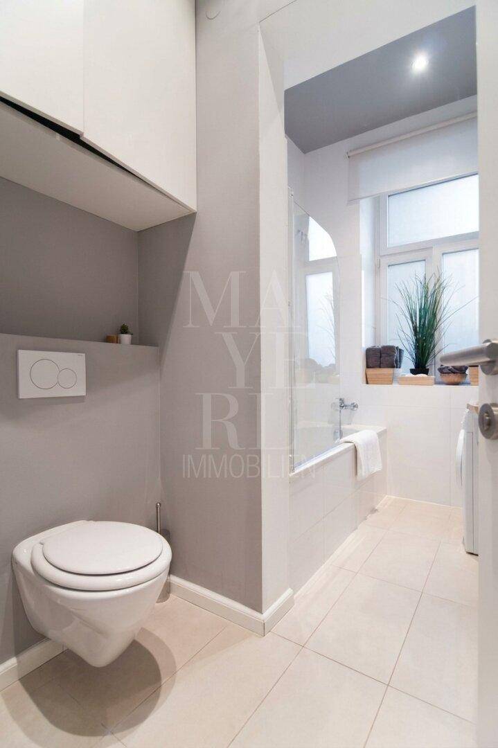 Modernes Badezimmer mit wandhängendem WC, Badewanne und Fenster für Tageslicht.