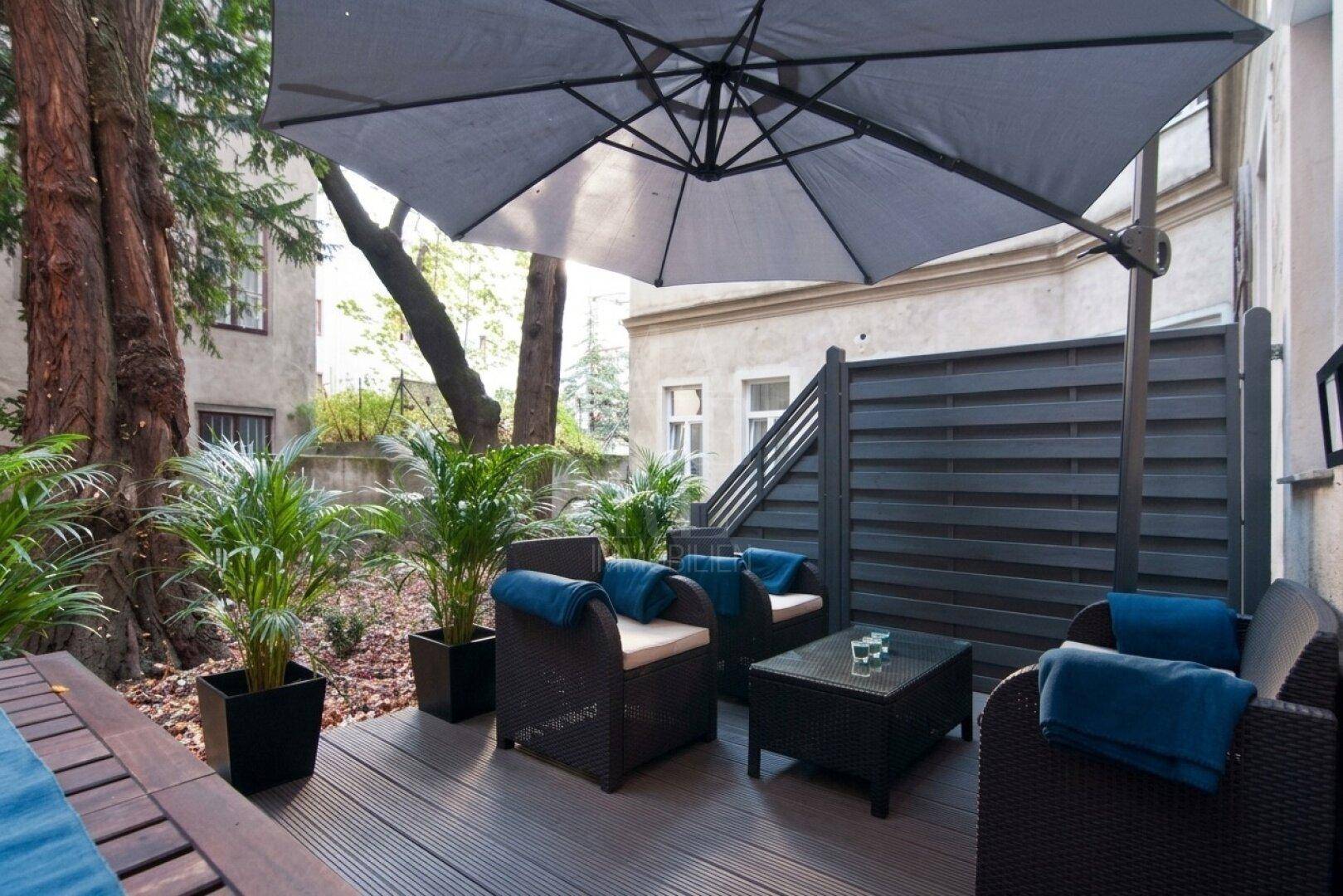 Gemütliche Terrasse im Innenhof mit Holzdeck, Sitzmöbeln und großem Sonnenschirm.