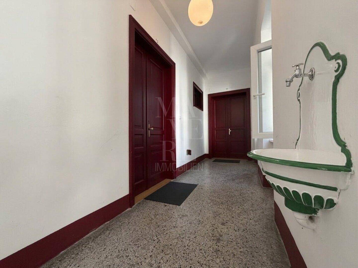 Historischer Flur mit Terrazzoboden und einem dekorativen Wandbrunnen in einem Altbau.