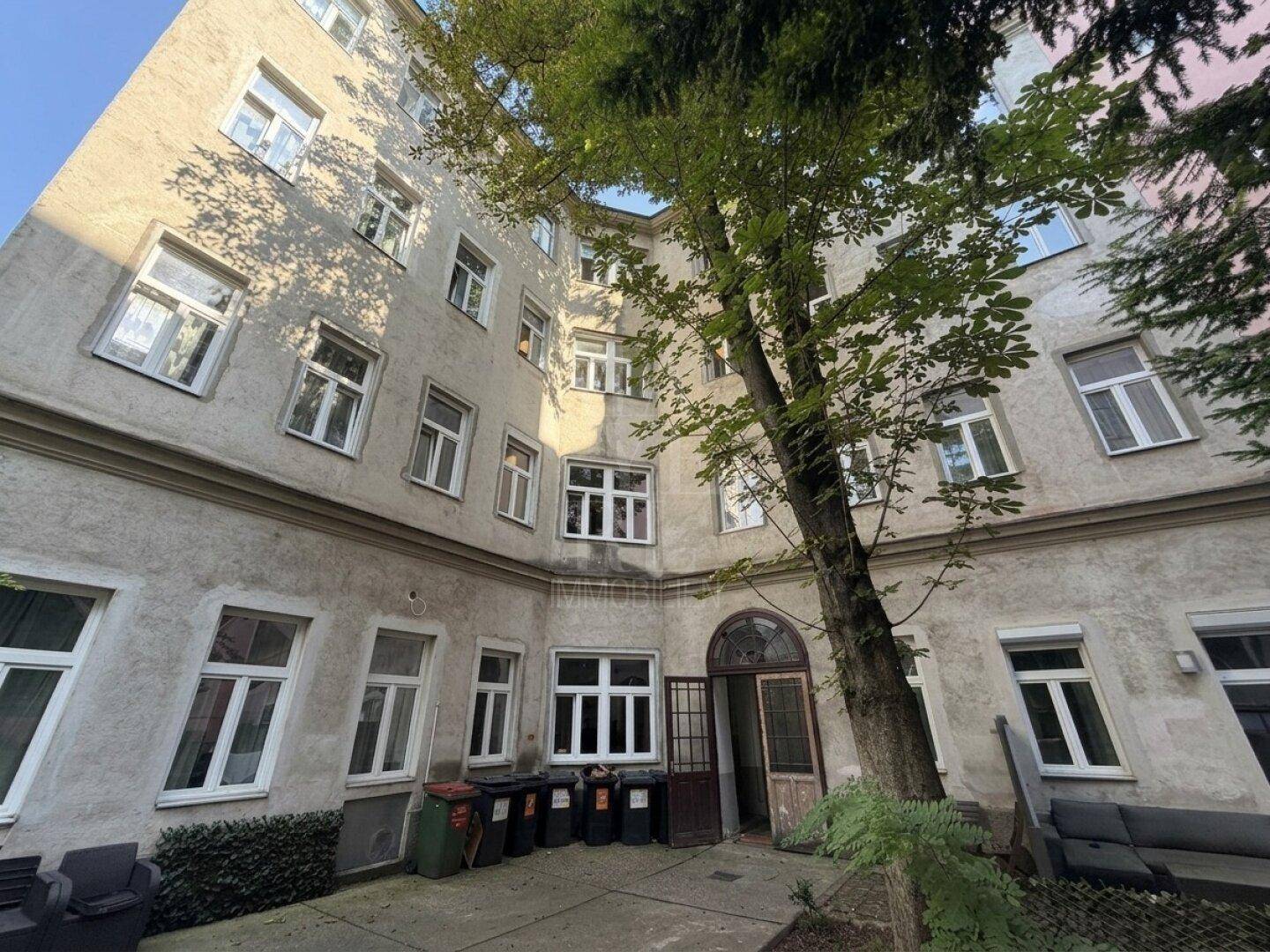Innenhof eines Altbaus mit Bäumen und Mülltonnen, umgeben von Wohnungen.