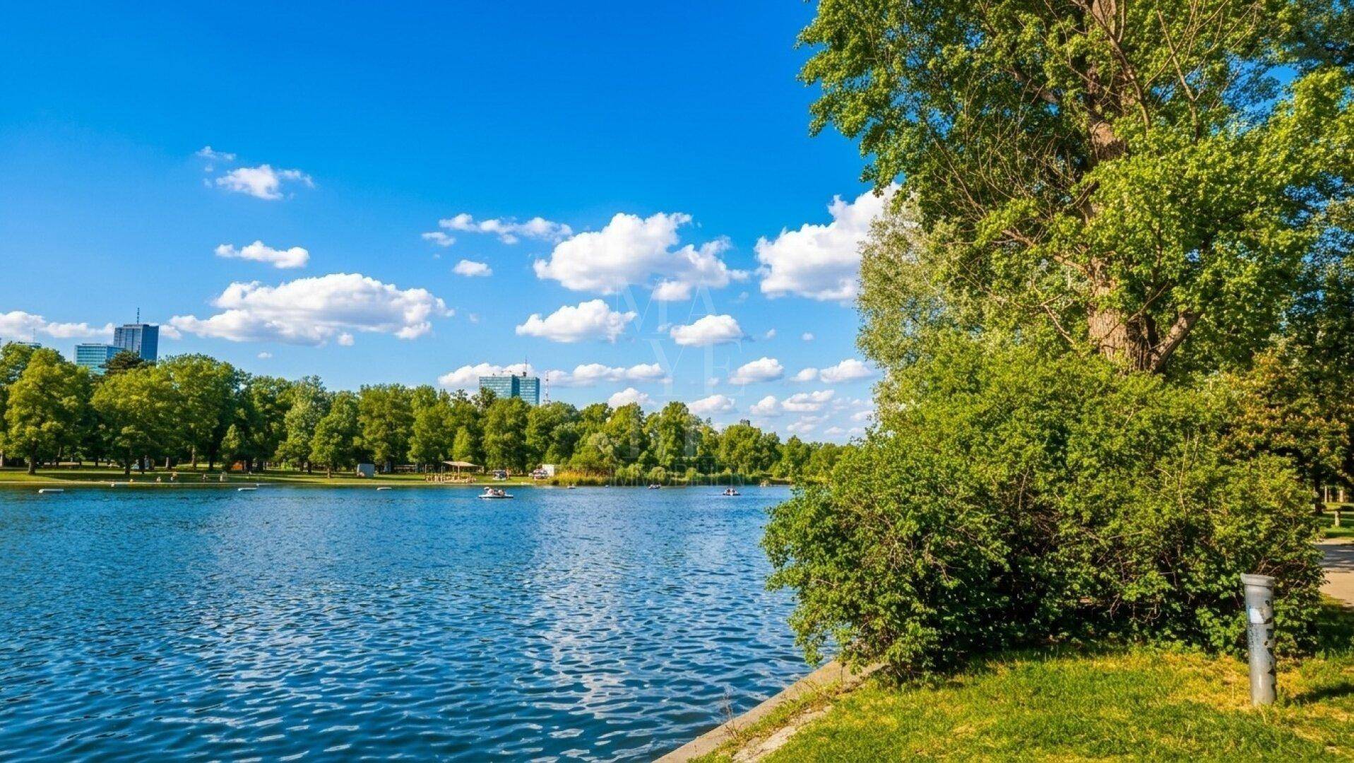 Weitläufiger See mit grünen Ufern und Blick auf die Stadtkulisse am Horizont.