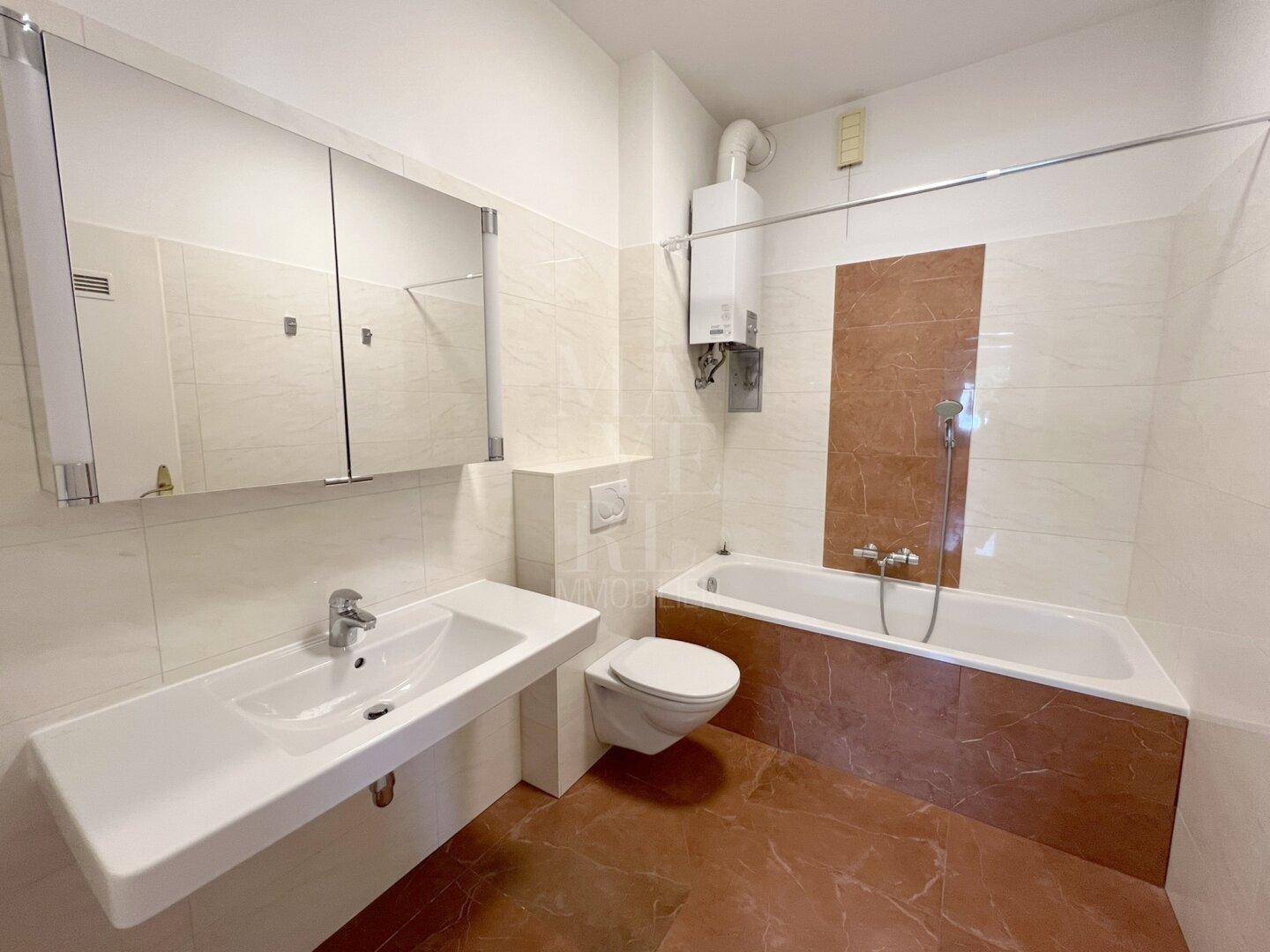Badezimmer mit Badewanne, WC, Waschbecken und hellen Fliesen in Beige- und Brauntönen.