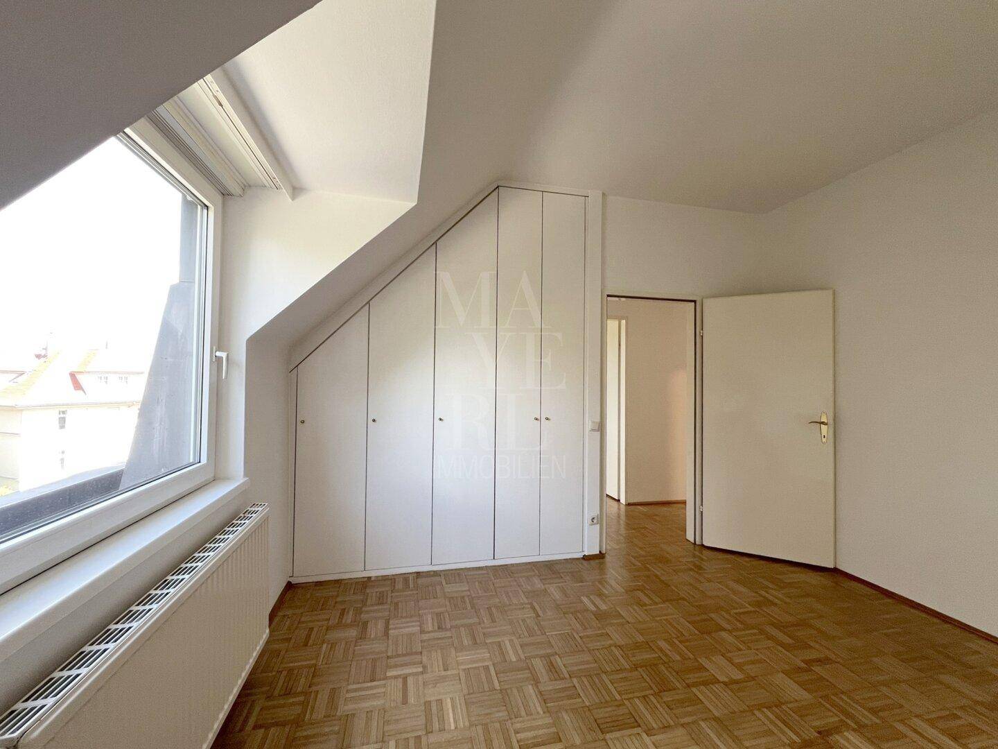 Schlafzimmer mit Parkettboden, Einbauschränken und Fenster, das den Raum hell erscheinen lässt.