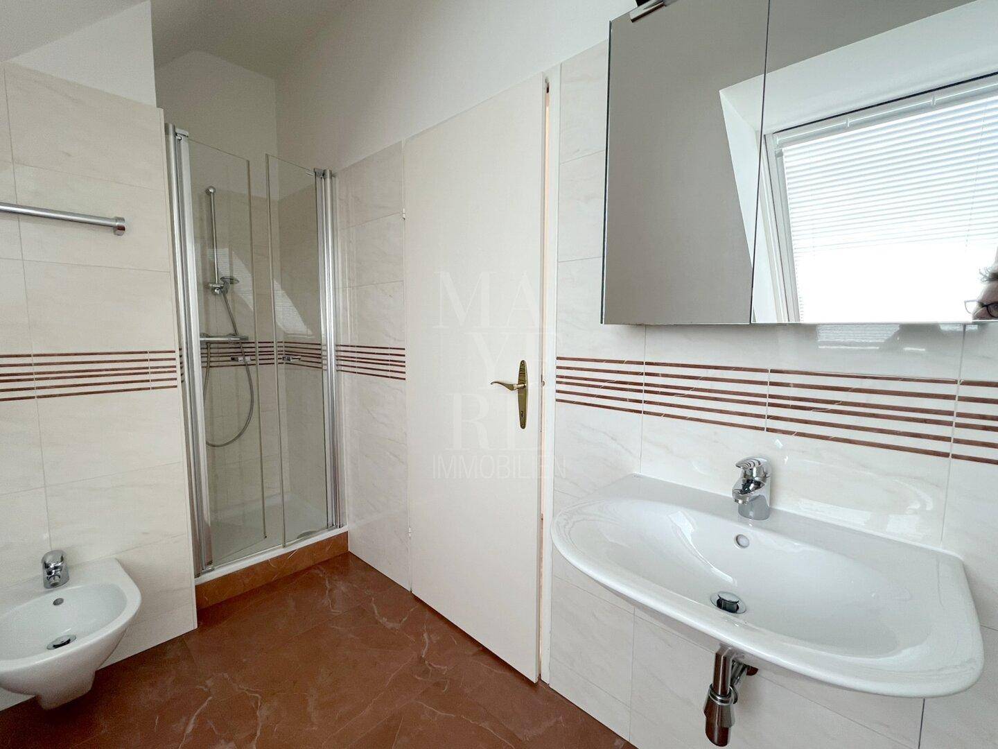 Badezimmer mit Dusche, Waschbecken, Bidet und Spiegelschrank unter einem Dachfenster.