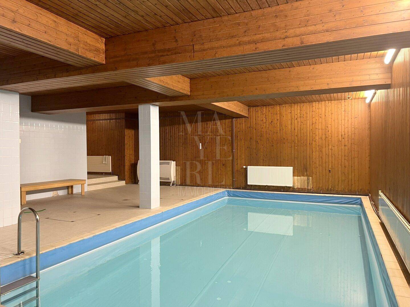 Innenpoolbereich mit Holzverkleidung, Schwimmbecken und Sitzgelegenheiten für Entspannung.
