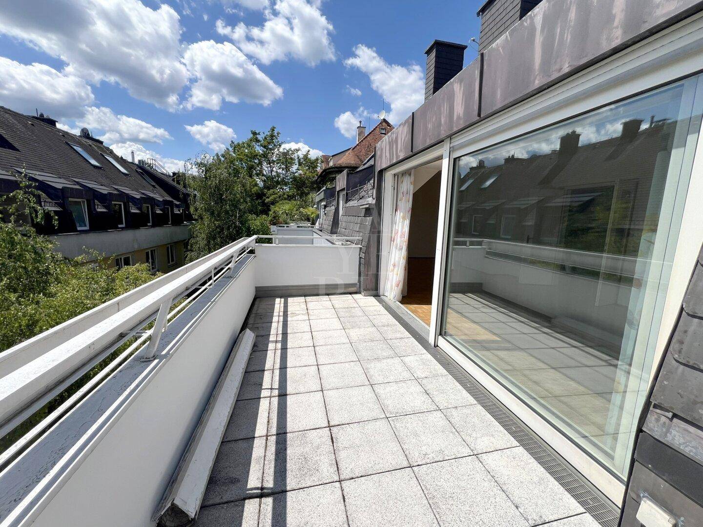 Geräumige Dachterrasse mit Fliesenboden und Blick auf die umliegenden Dächer und Bäume.