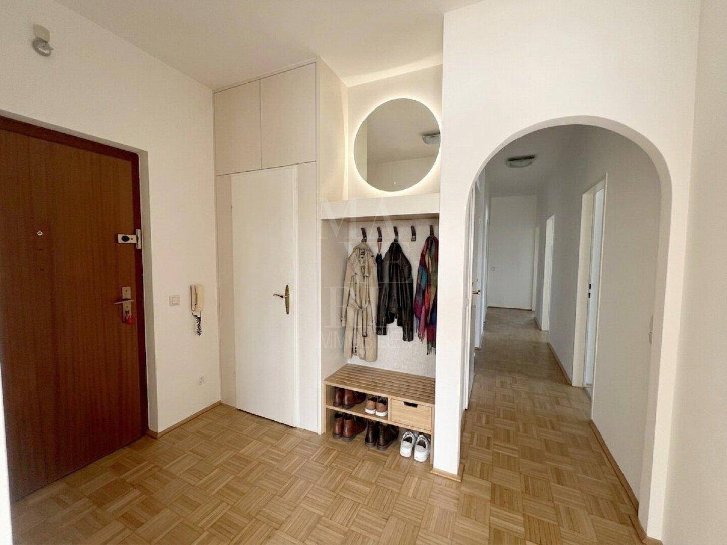 Heller Eingangsbereich mit Garderobe, Spiegel und Parkettboden, der zu den weiteren Räumen führt.
