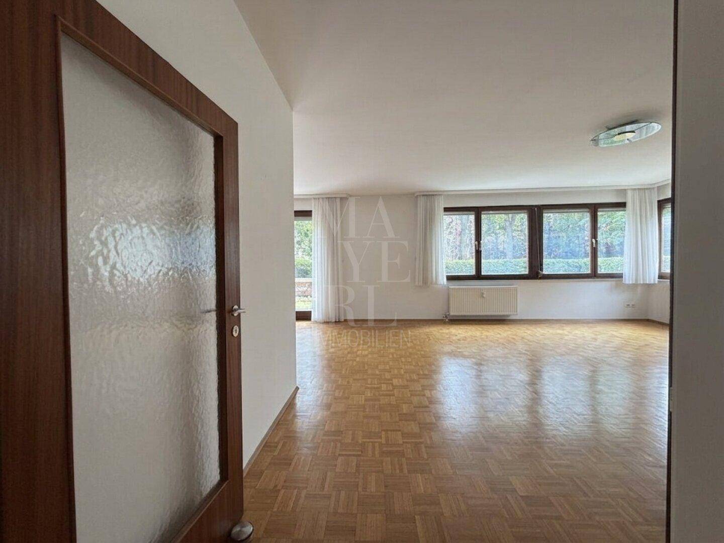 Helles Wohnzimmer mit Parkettboden und Blick ins Grüne durch große Fenster.