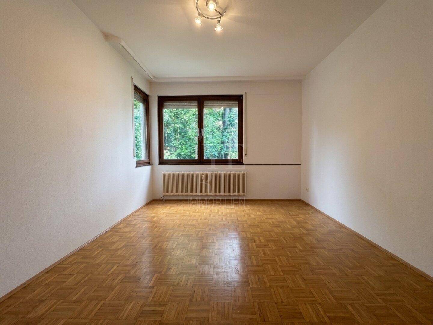 Helles Schlafzimmer mit Parkettboden und Blick ins Grüne.