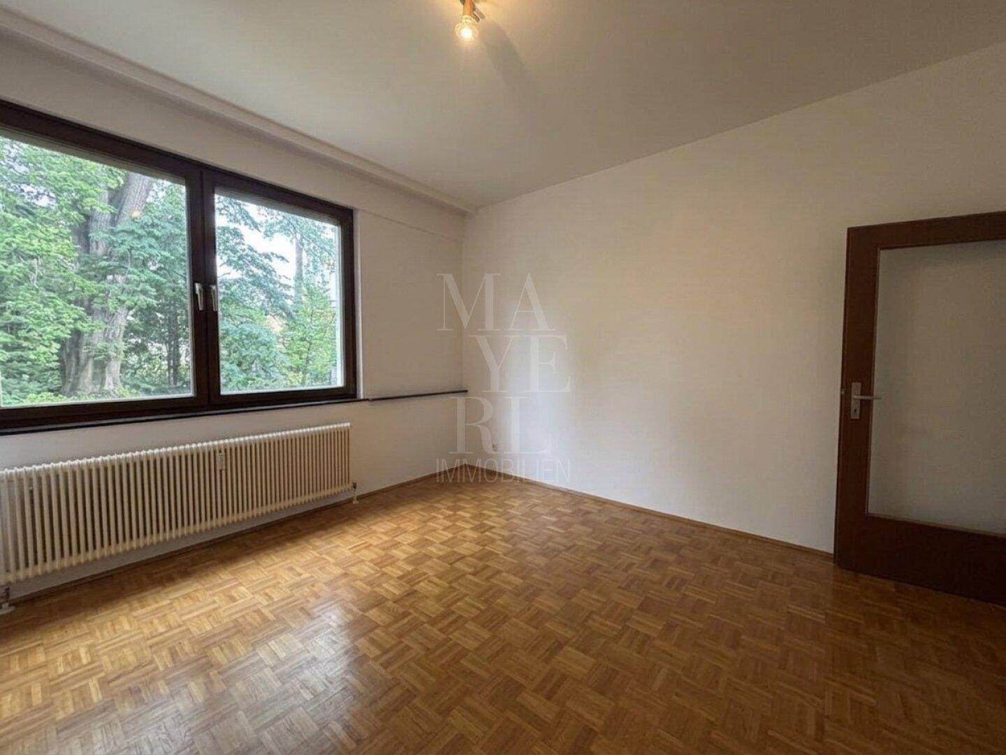 Geräumiges Schlafzimmer mit Parkettboden und Fenster mit Blick auf Bäume.