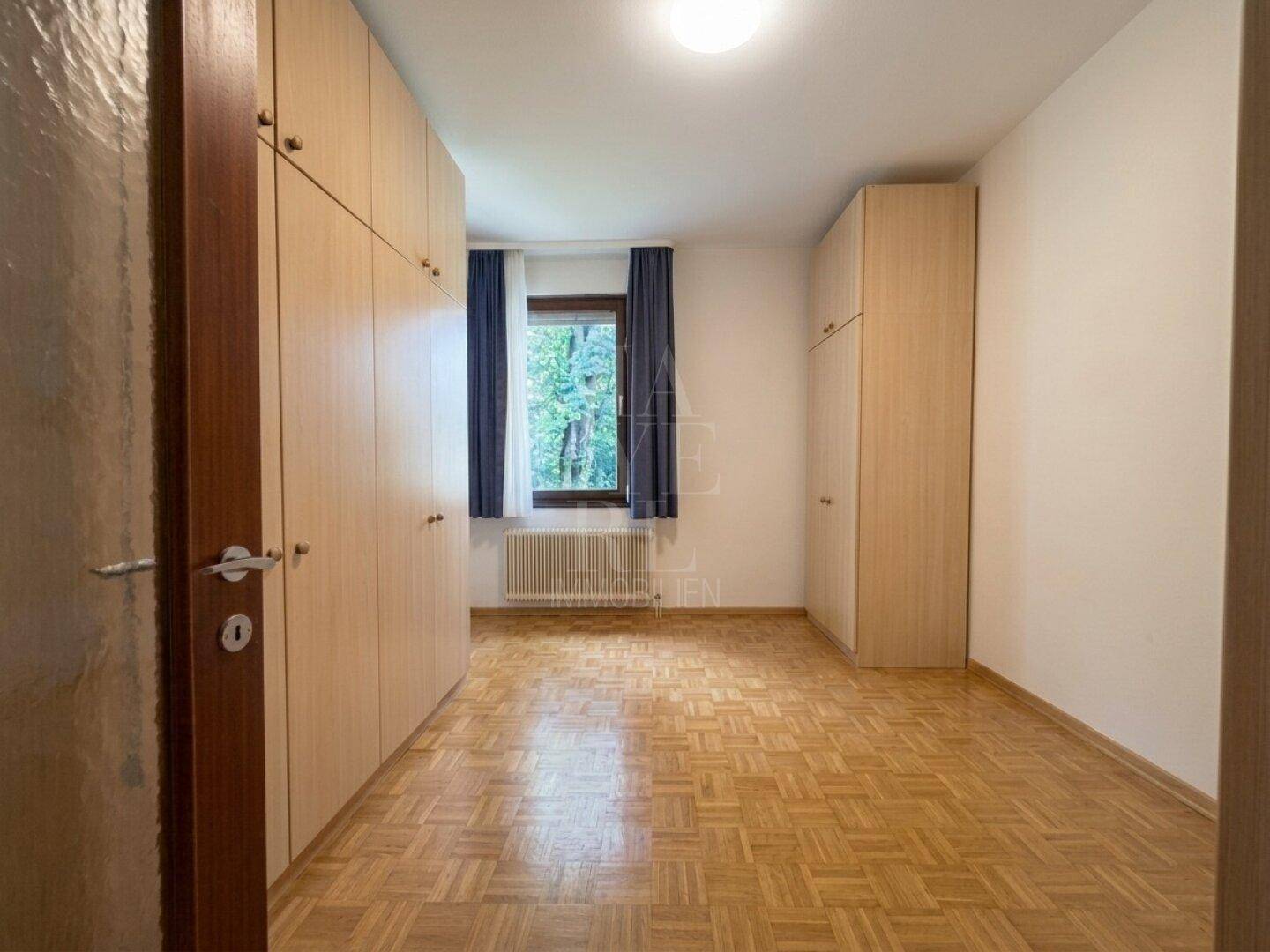 Schlafzimmer mit Einbauschränken, Parkettboden und Fenster.