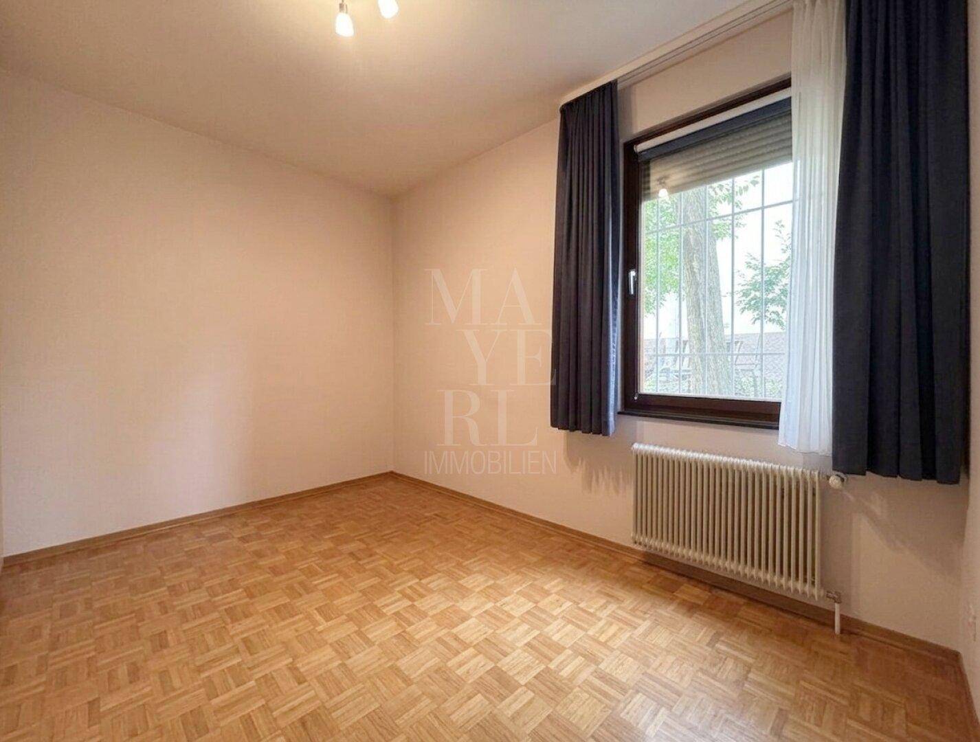 Helles Schlafzimmer mit Parkettboden und Fenster mit Blick ins Grüne.