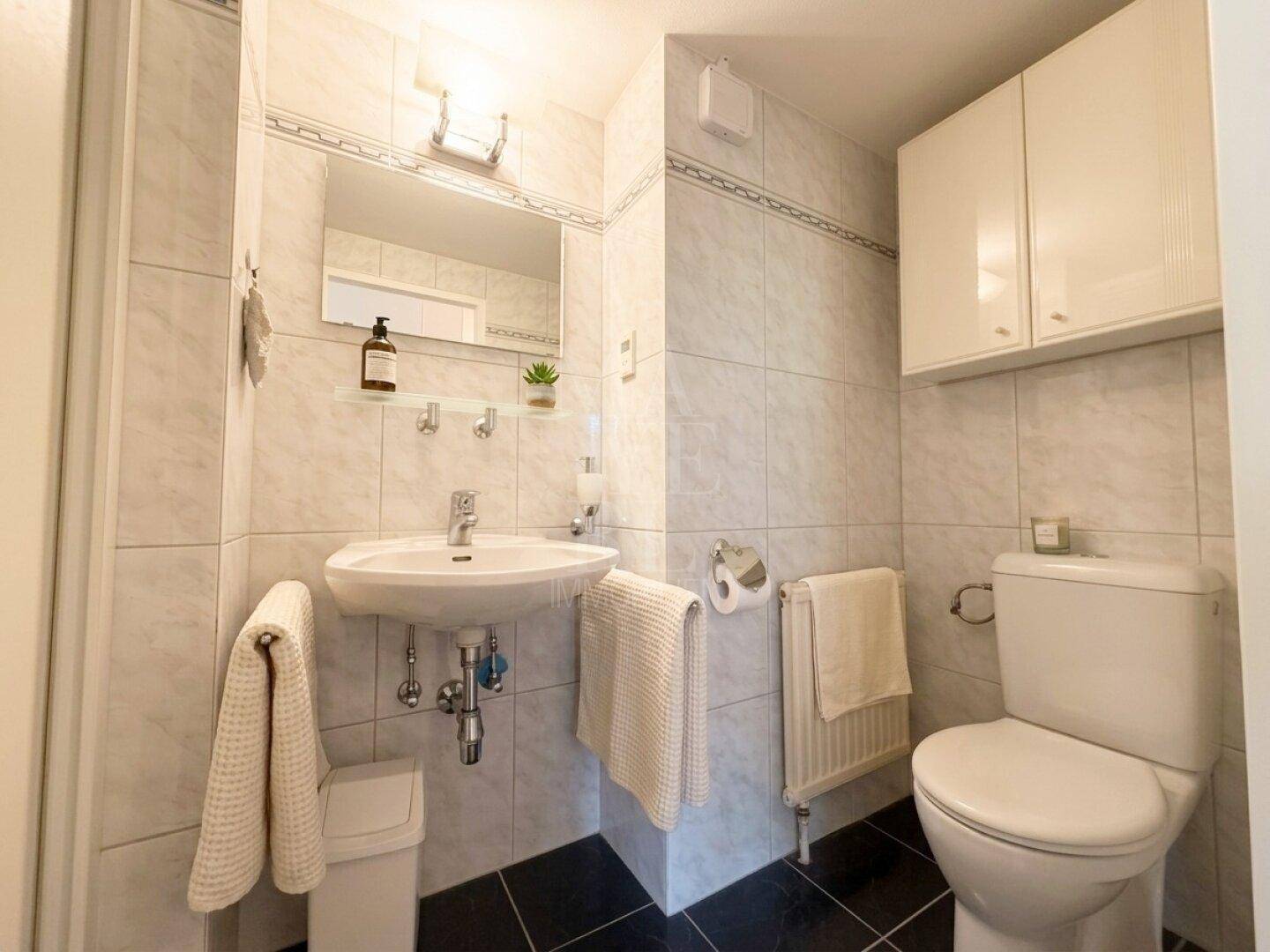 Gäste-WC mit Waschbecken, Toilette und hellen Fliesen.