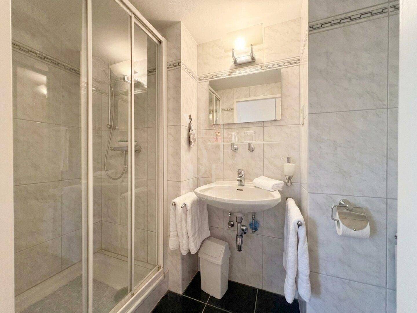 Badezimmer mit Duschkabine, Waschbecken und hellen Fliesen.