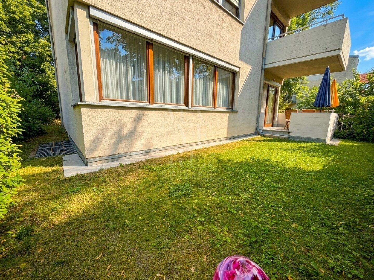 Grüne Rasenfläche neben dem Gebäude mit Fenstern und Zugang zur Terrasse.