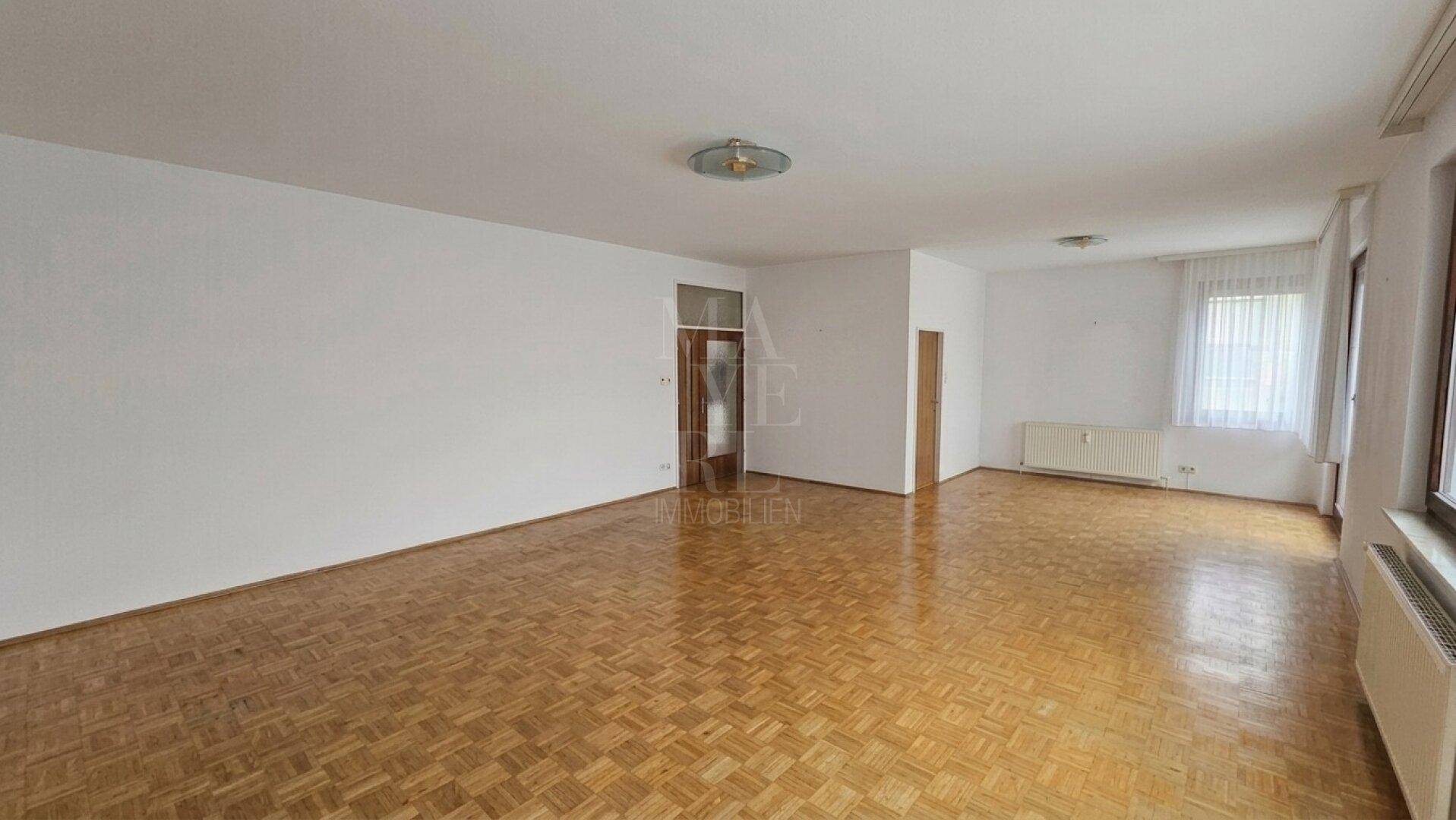 Leeres Wohnzimmer mit Parkettboden und großen Fenstern, bereit zur Einrichtung.