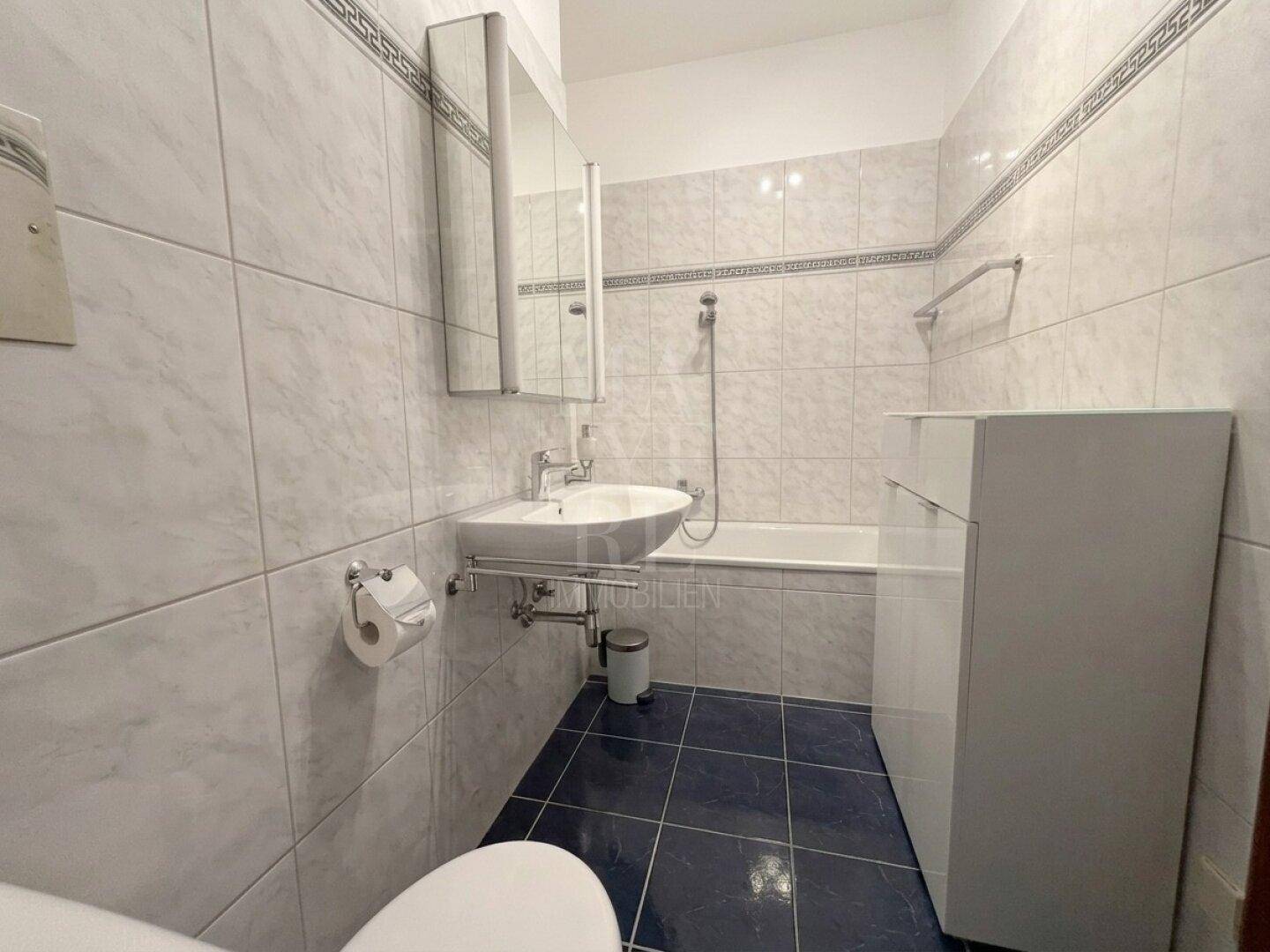 Badezimmer mit Badewanne, Waschbecken und hellen Fliesen.