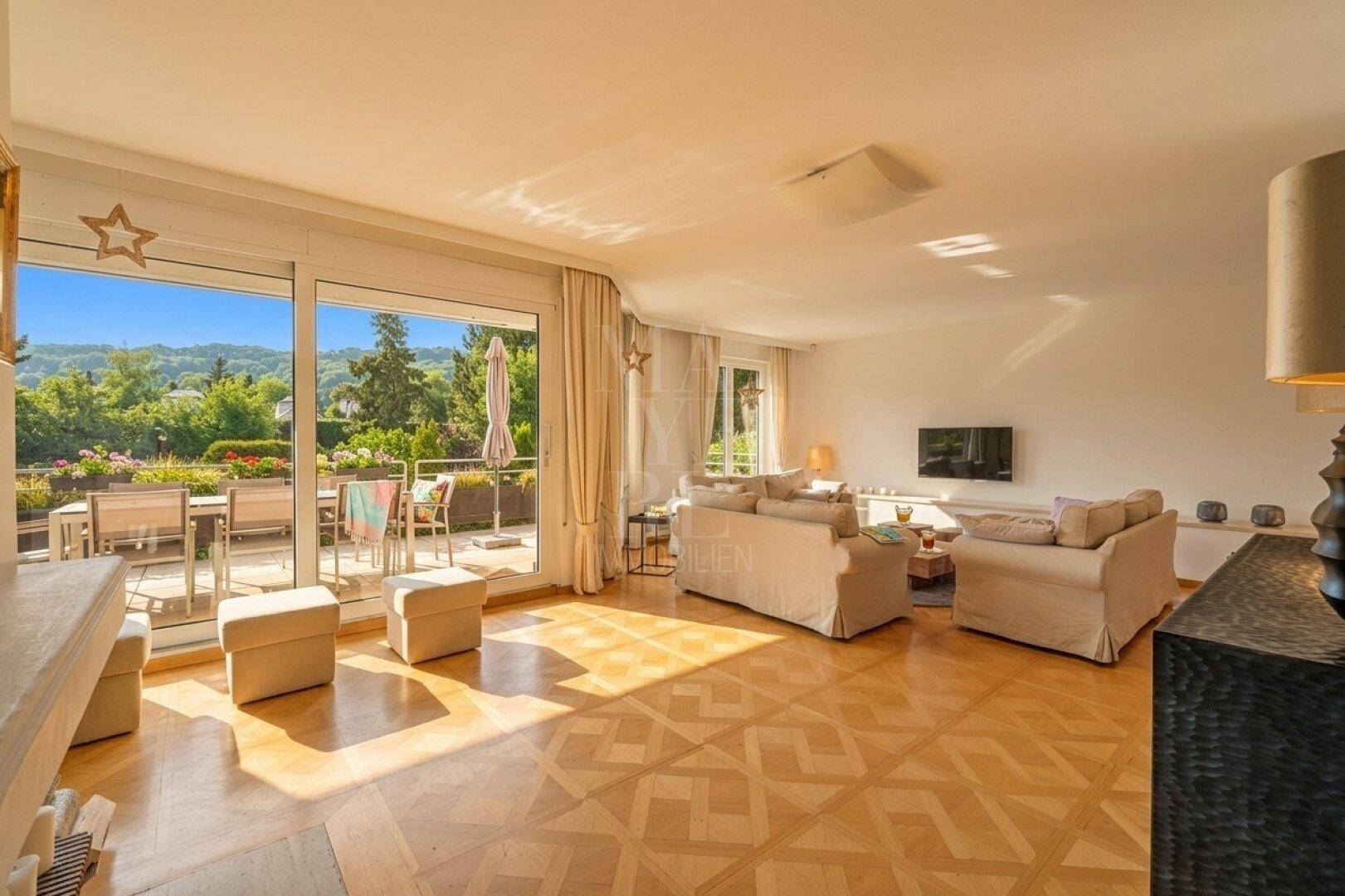 Helles Wohnzimmer mit Parkettboden, beigen Sofas und Zugang zu einer großen Terrasse mit Bergblick.