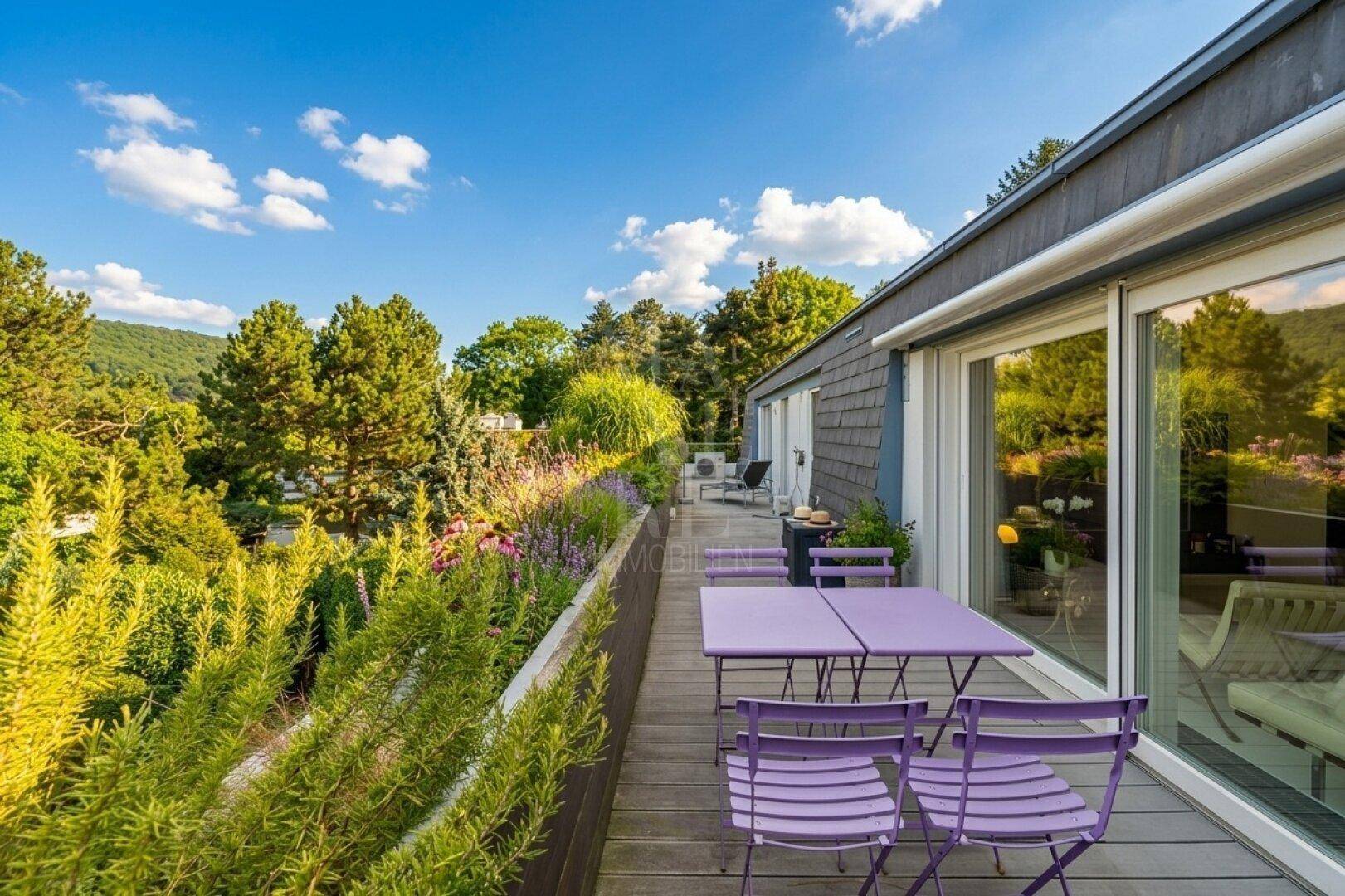Sonniger Balkon mit Holzbelag, lila Gartenmöbeln und weitem Blick über die grüne Landschaft.