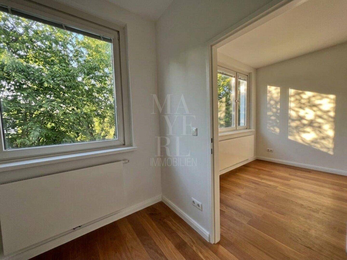 Lichtdurchfluteter Raum mit Holzboden und großem Fenster, das viel Tageslicht hereinlässt.