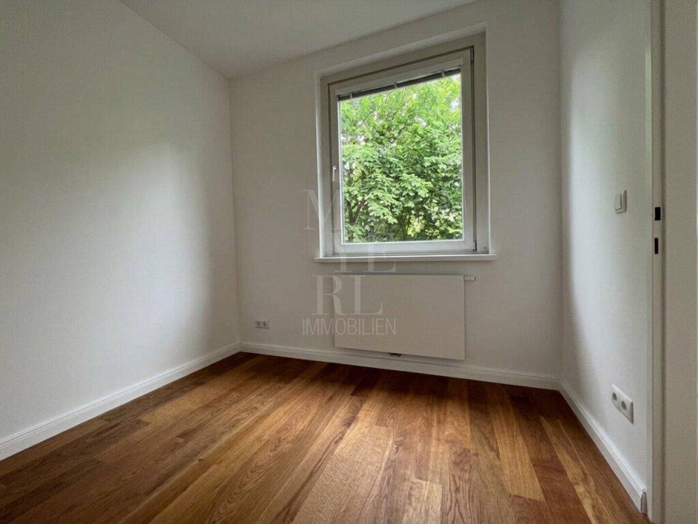 Kleineres Zimmer mit Holzboden und Fenster, das einen Blick ins Grüne bietet.