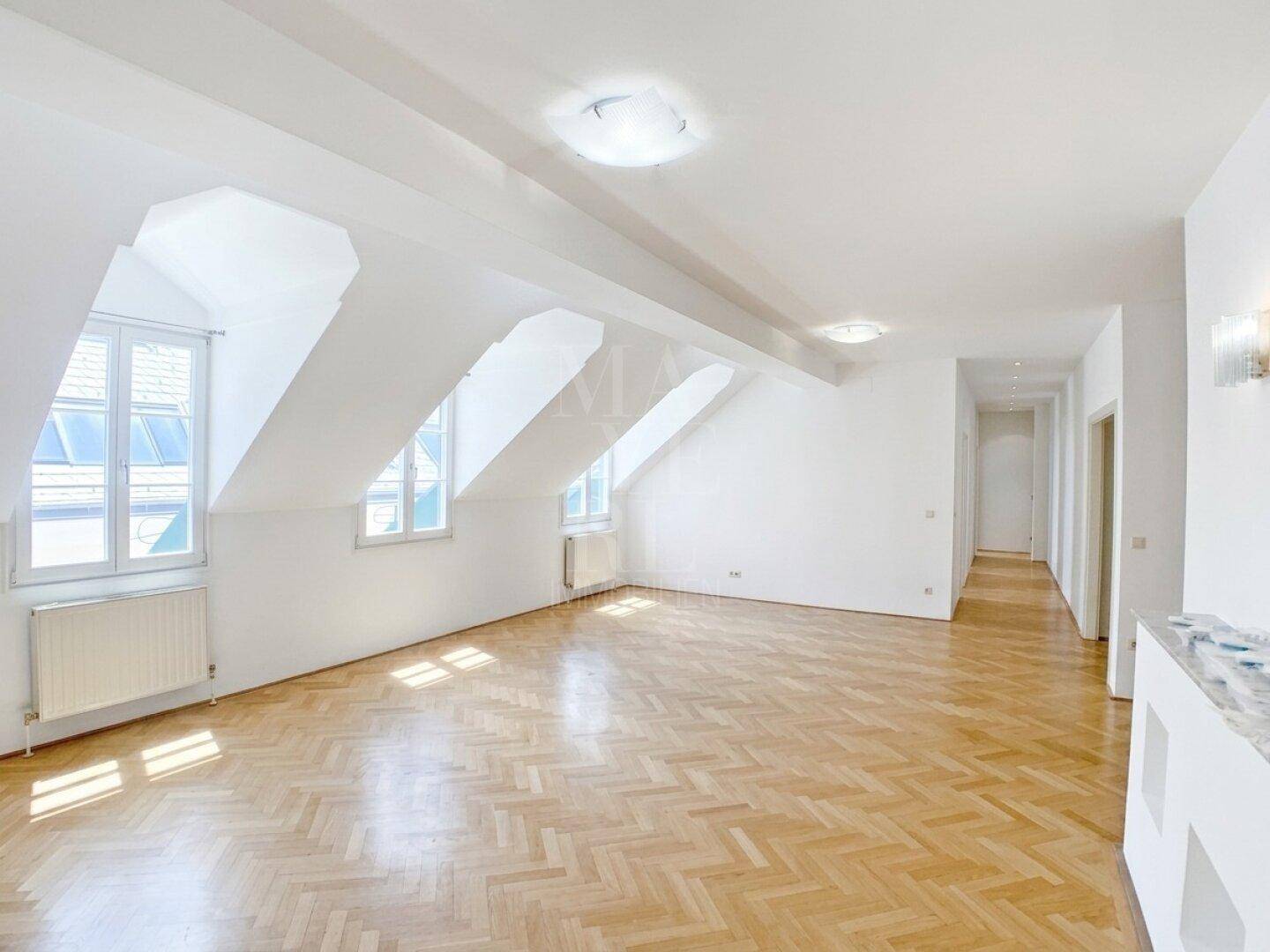 Heller Wohnraum mit Fischgrätparkett, Dachschrägen und großen Gaubenfenstern.