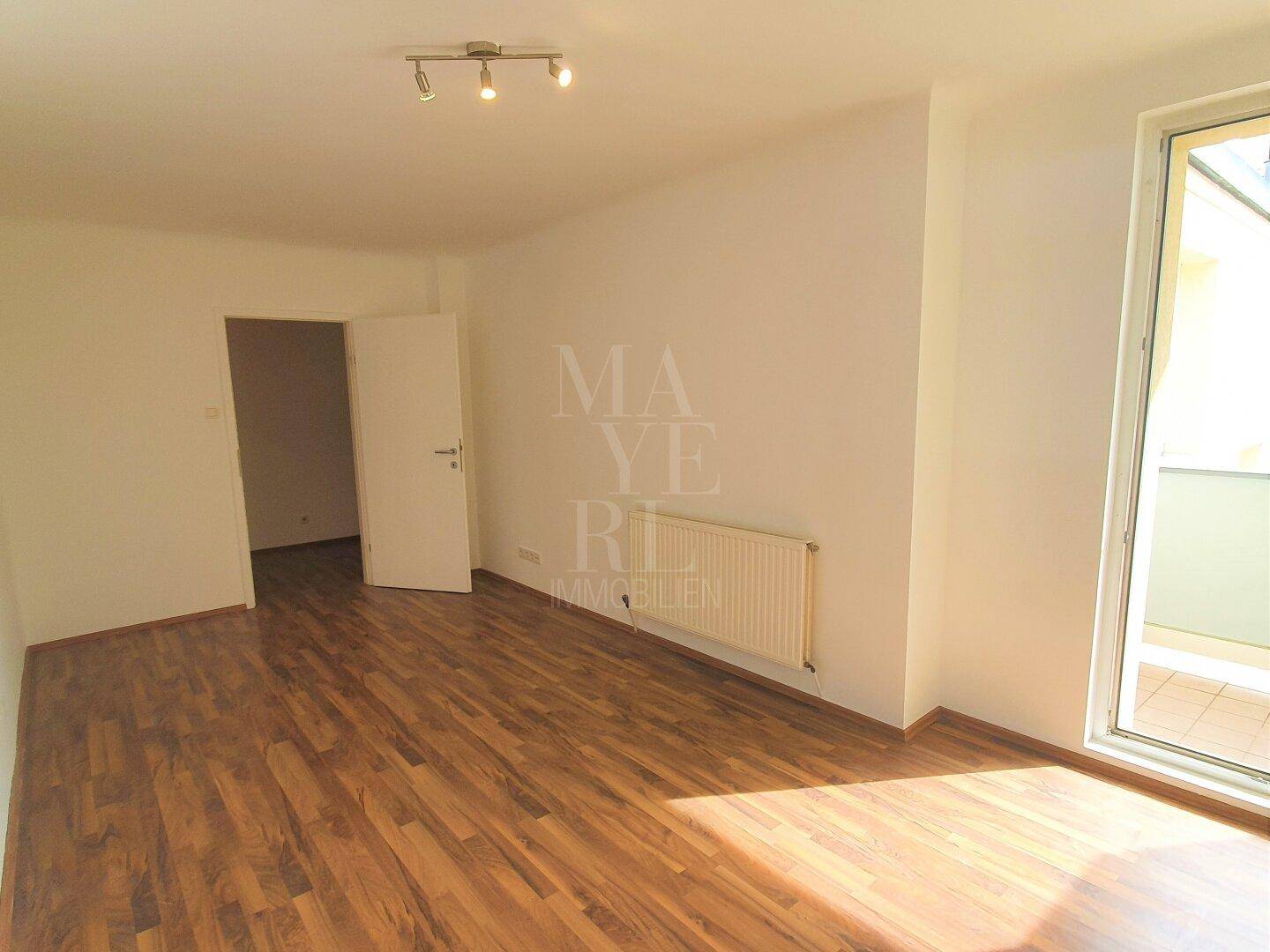 Heller Raum mit Parkettboden, weißen Wänden und Zugang zu einem Balkon, gut gepflegt.