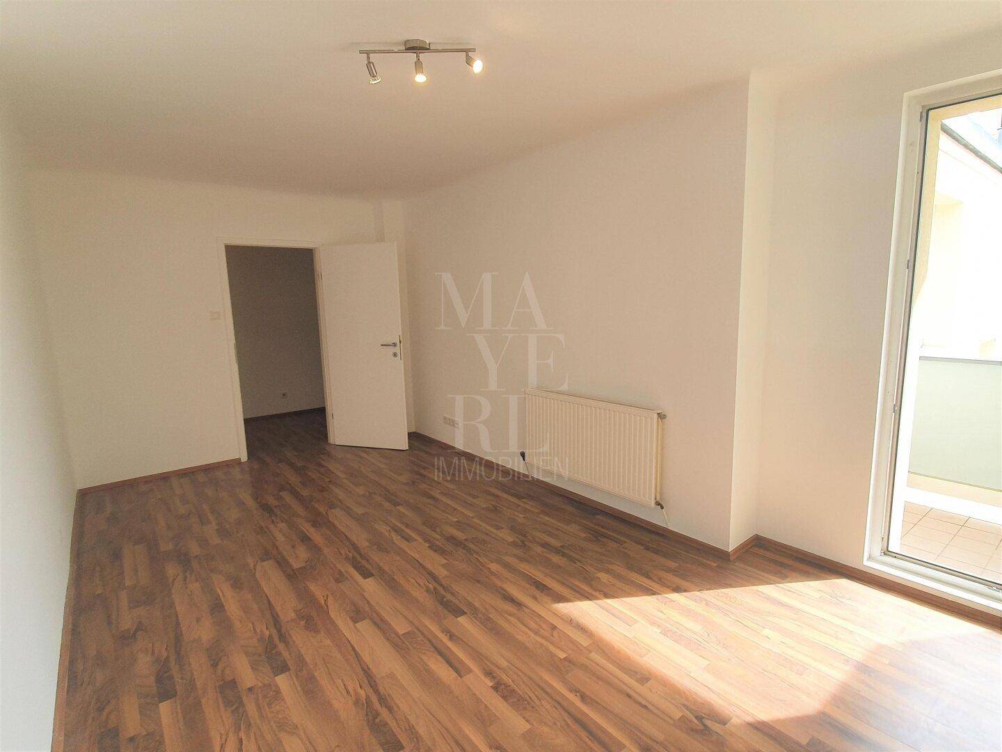 Heller Raum mit Parkettboden, weißen Wänden und Zugang zu einem Balkon, gut gepflegt.