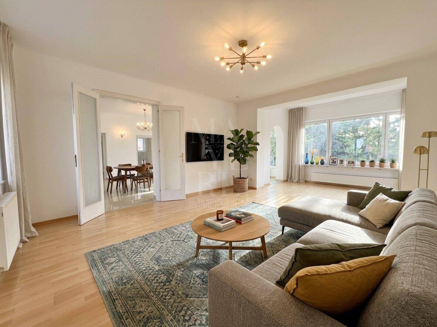 Gemütliches Wohnzimmer mit Sofa, Couchtisch und Parkettboden, durch große Fenster lichtdurchflutet.