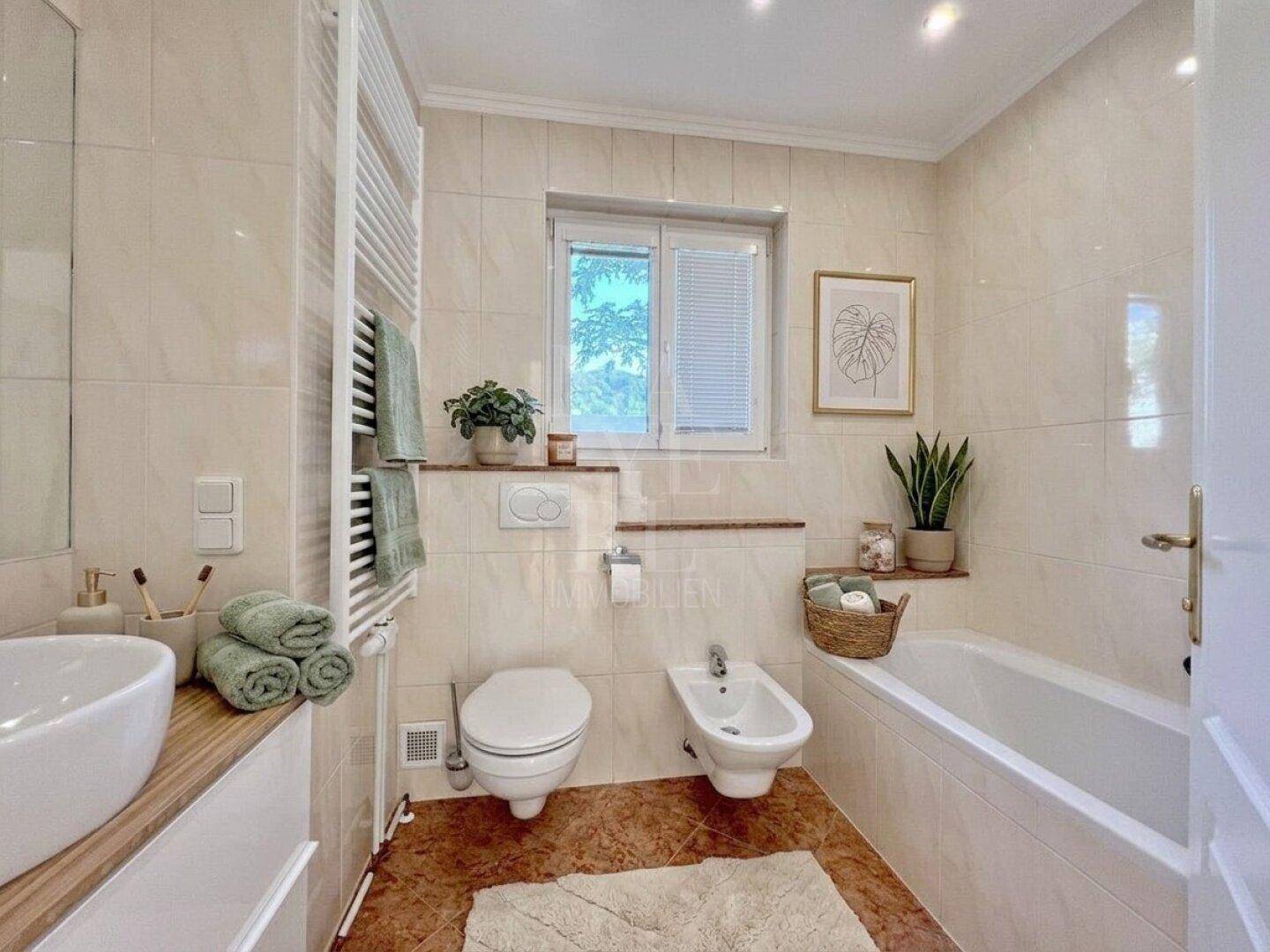 Freundliches Badezimmer mit Badewanne, Bidet und Einzelwaschbecken, dekoriert mit Pflanzen.