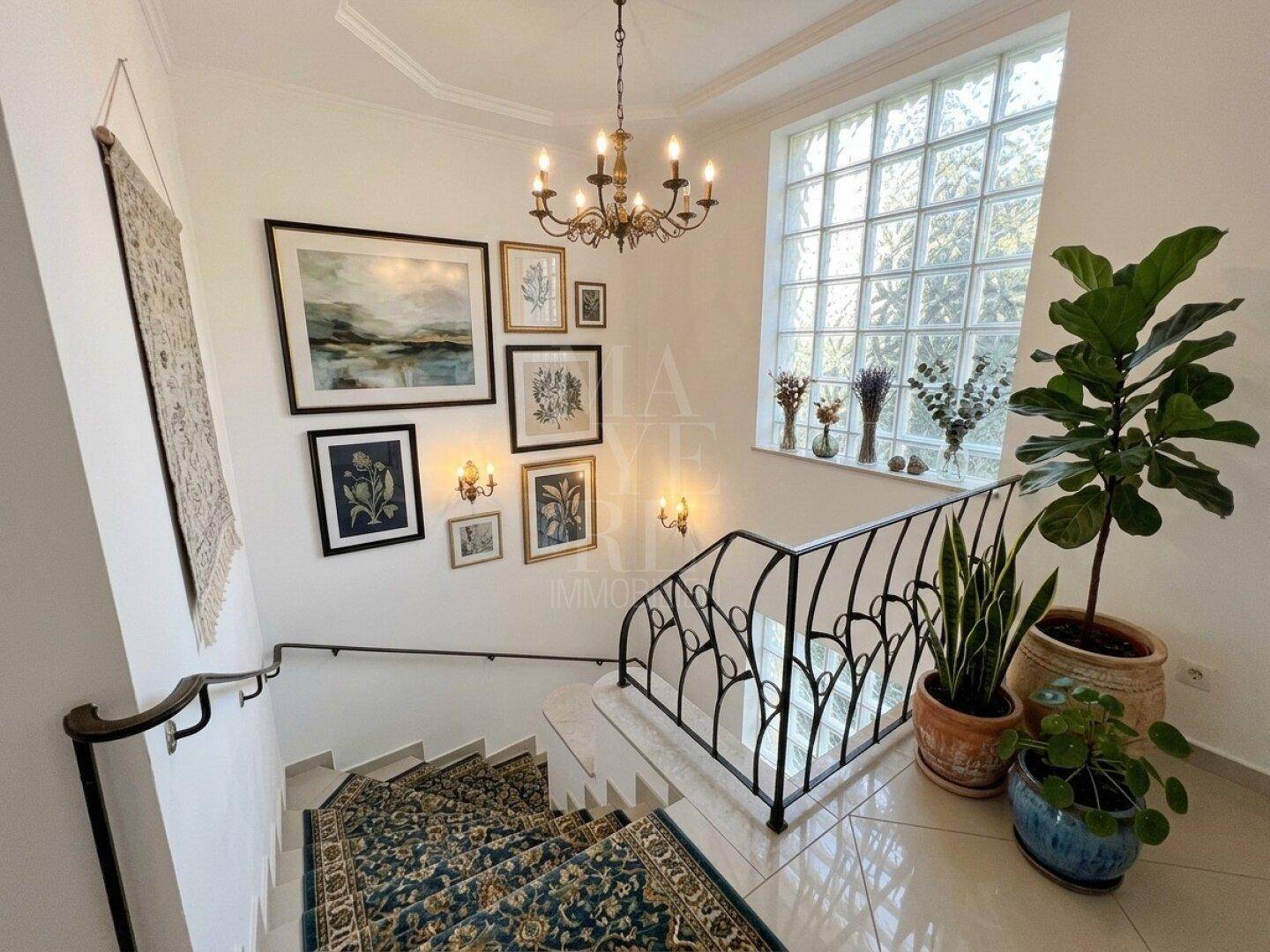 Elegantes Treppenhaus mit schmiedeeisernem Geländer, Teppichboden und dekorativen Bildern an der Wand.