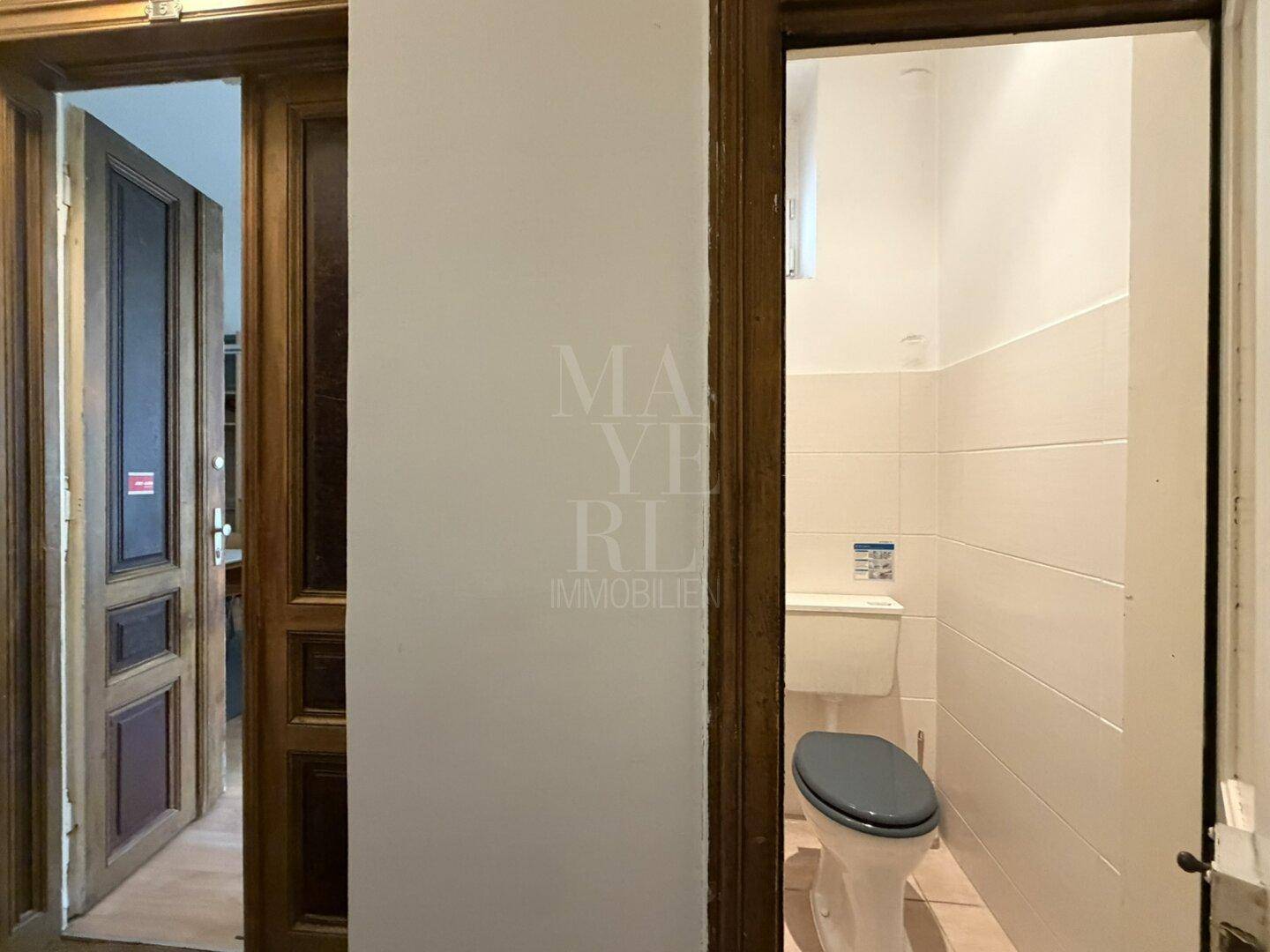 Eine einfache Toilette mit weiß gefliesten Wänden und einem kleinen Fenster.