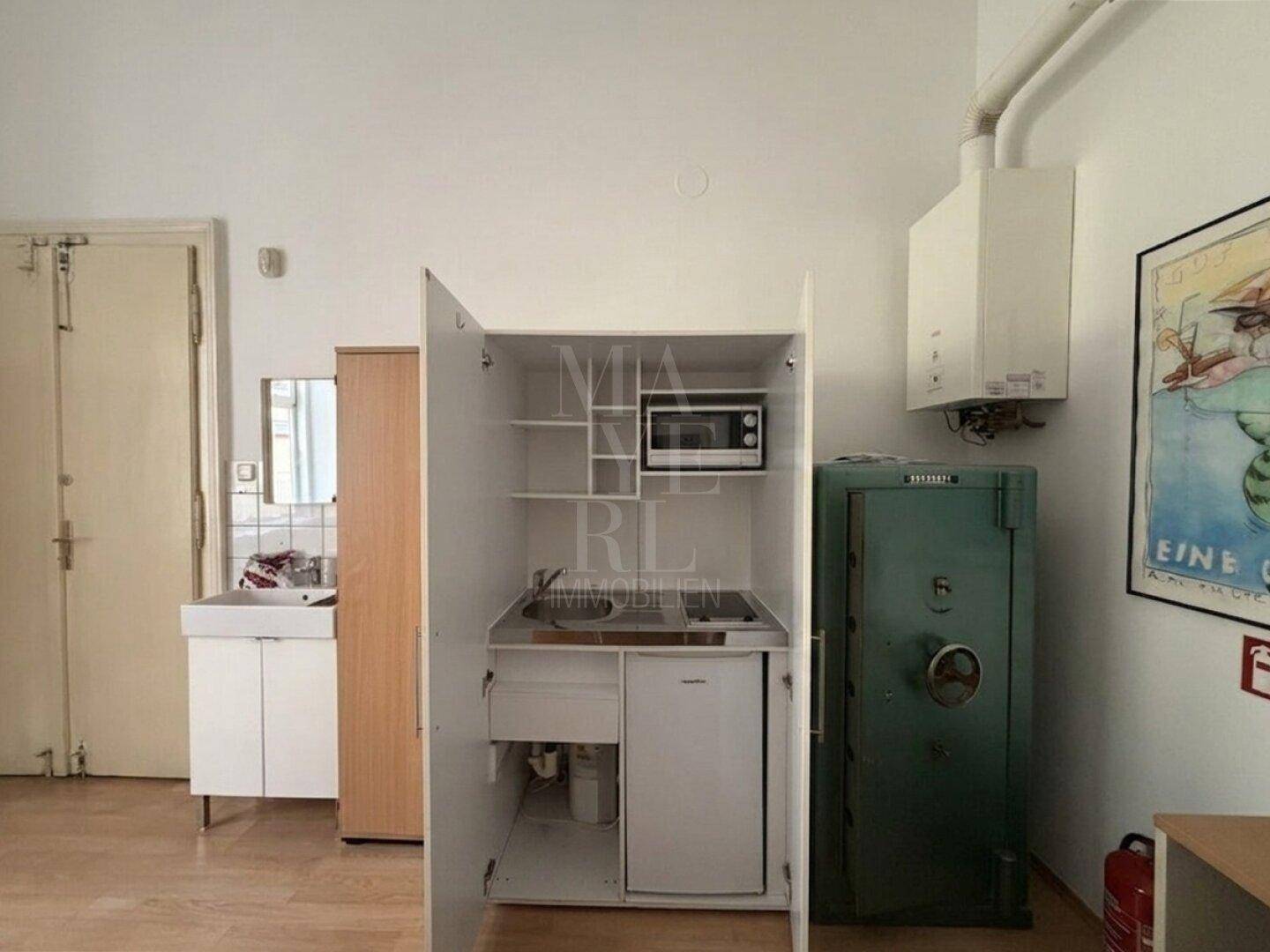 Eine kleine Küchenzeile mit Mikrowelle und Kühlschrank, daneben ein großer Tresor.