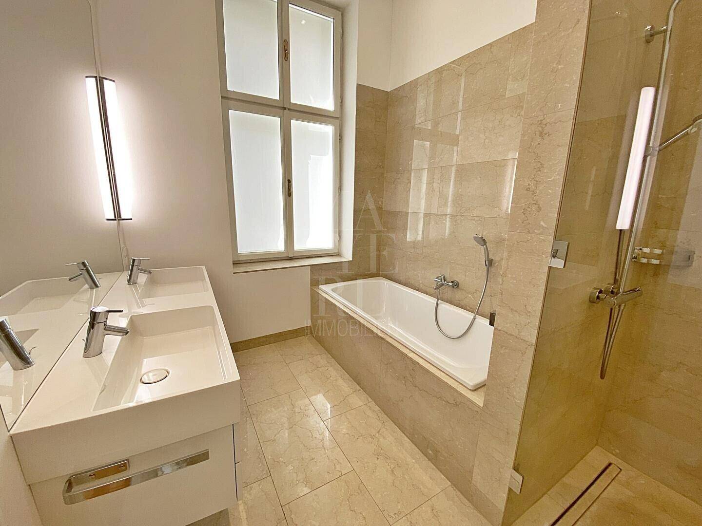 Modernes Badezimmer mit Doppelwaschbecken, Badewanne und beigefarbenen Fliesen.