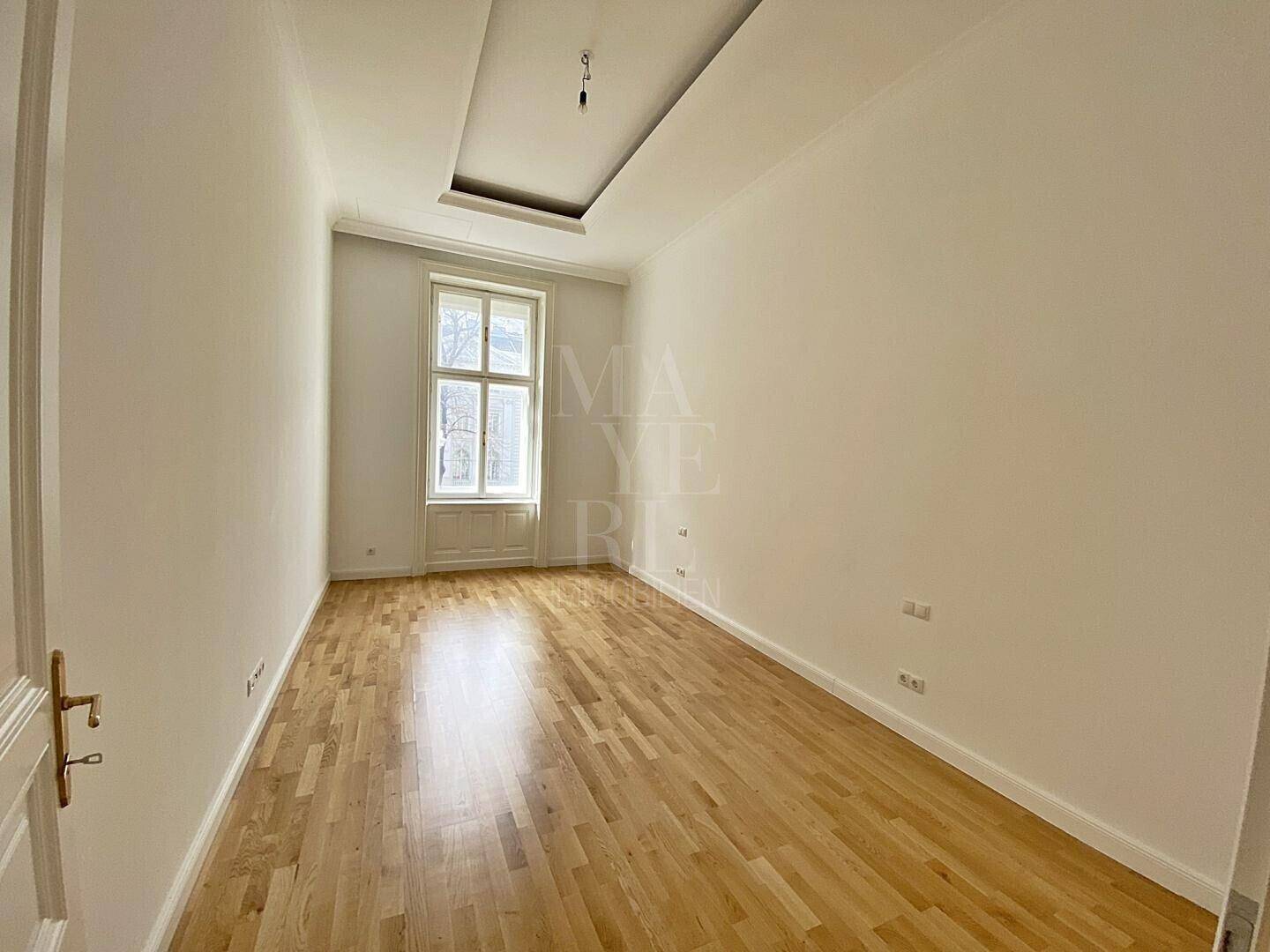 Helles Schlafzimmer mit Parkettboden, hohen Decken und großem Fenster.