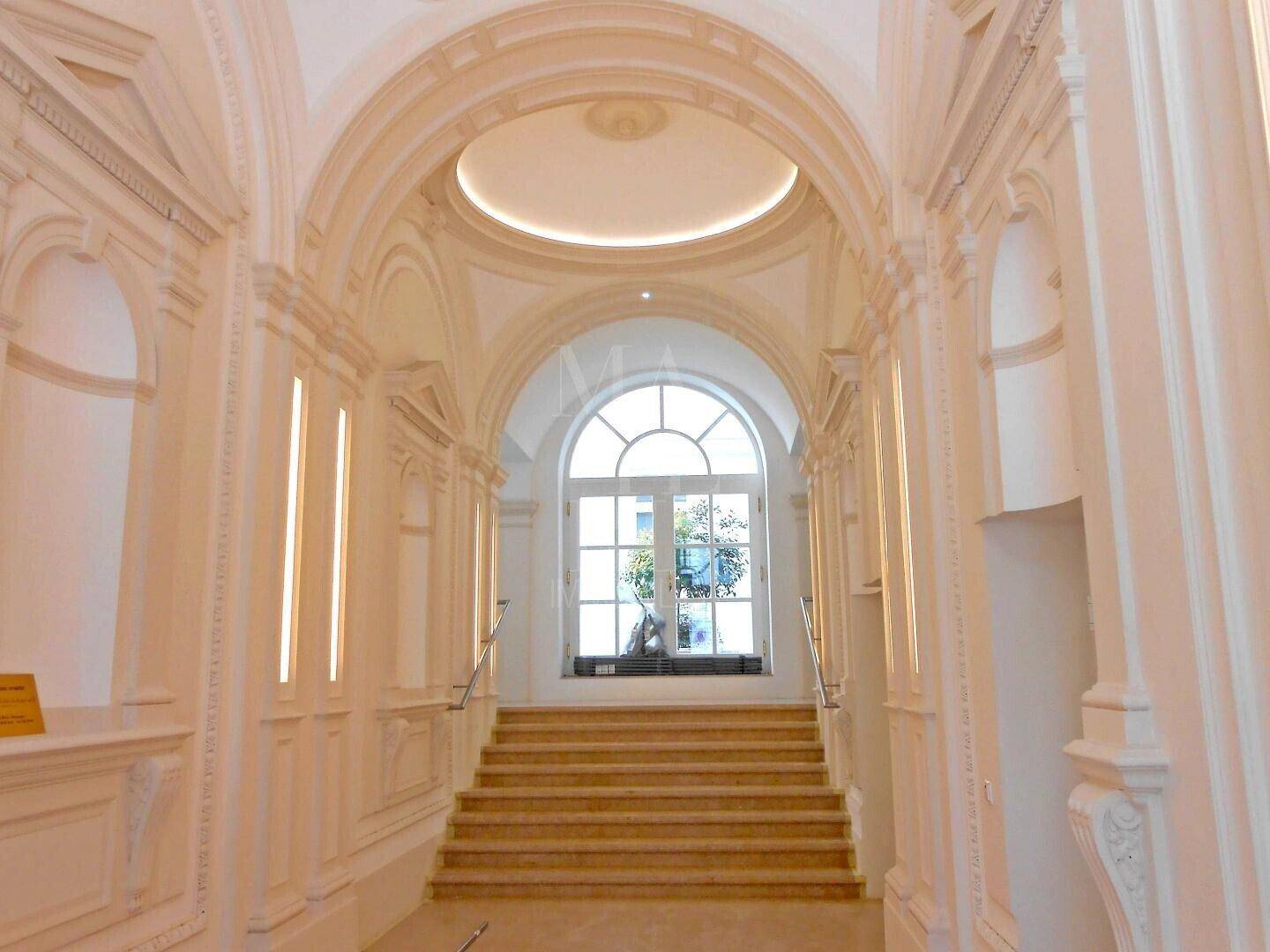 Prunkvolles Treppenhaus mit Stuckverzierungen, hohen Bögen und natürlichem Lichteinfall.