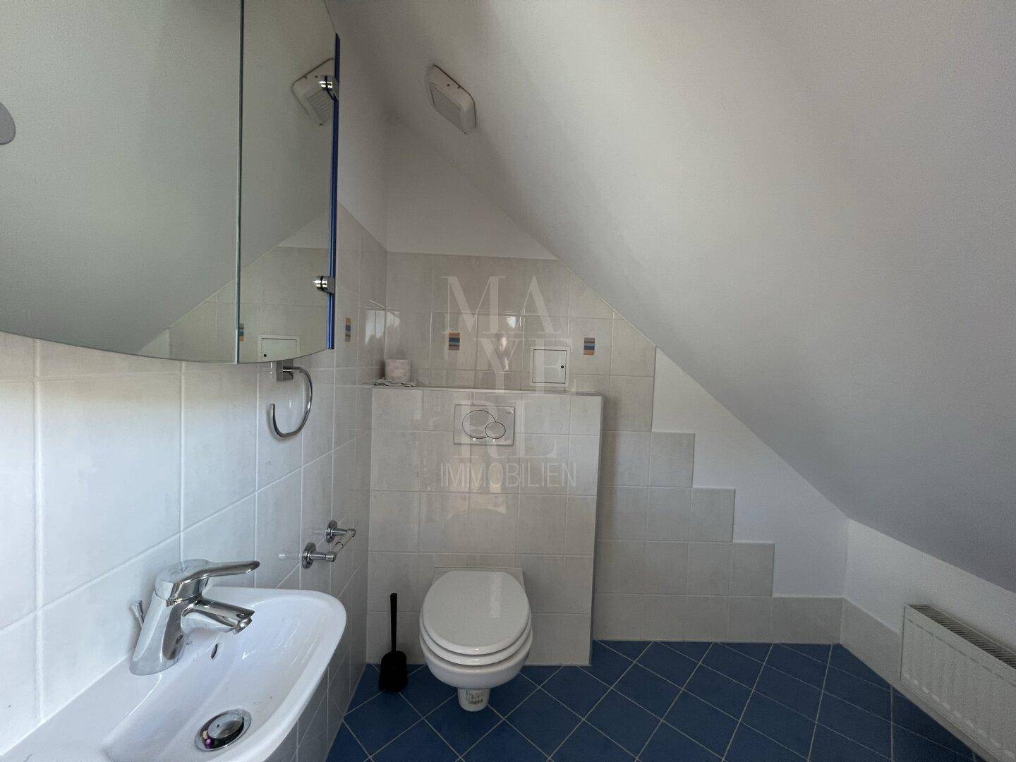 Dachgeschoss-Badezimmer mit WC, Waschbecken, blauen Fliesen und Dachschrägen.