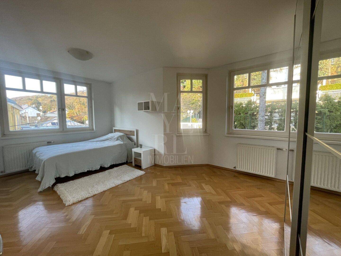Geräumiges Schlafzimmer mit Parkettboden, Einzelbett und großen Fenstern für viel Tageslicht.