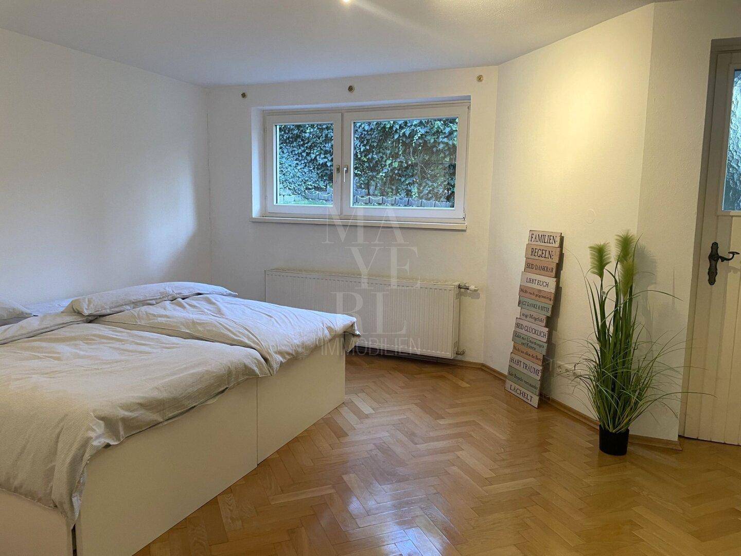 Helles Zimmer im Untergeschoss mit Parkettboden, Doppelbett und Blick ins Grüne.