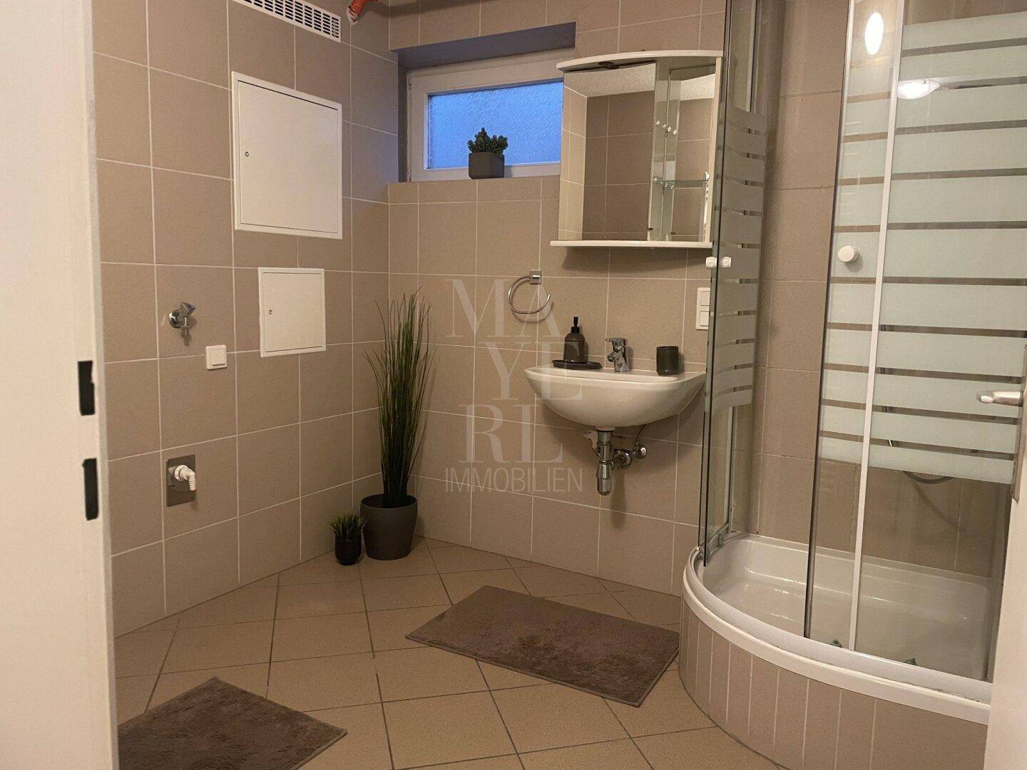 Modernes Badezimmer im Untergeschoss mit Dusche, Waschbecken und beigefarbenen Fliesen.