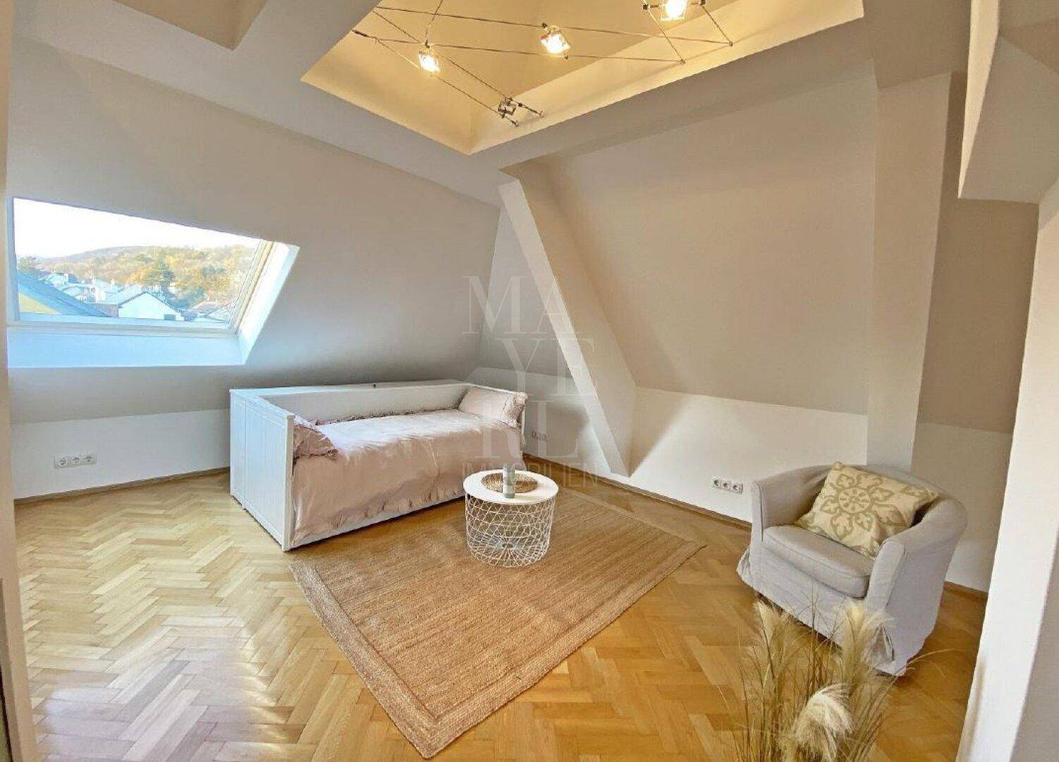 Helles Dachgeschoss-Schlafzimmer mit Dachfenster, Parkettboden und gemütlicher Sitzecke.