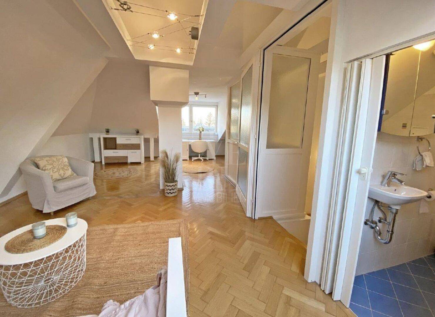 Offener Dachgeschossraum mit Parkettboden und direktem Zugang zu einem Badezimmer.