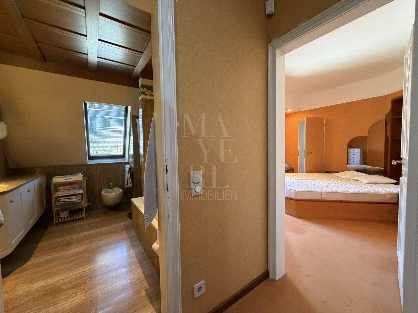 Blick vom Schlafzimmer in das angrenzende Badezimmer mit Holzboden und Dachfenster.